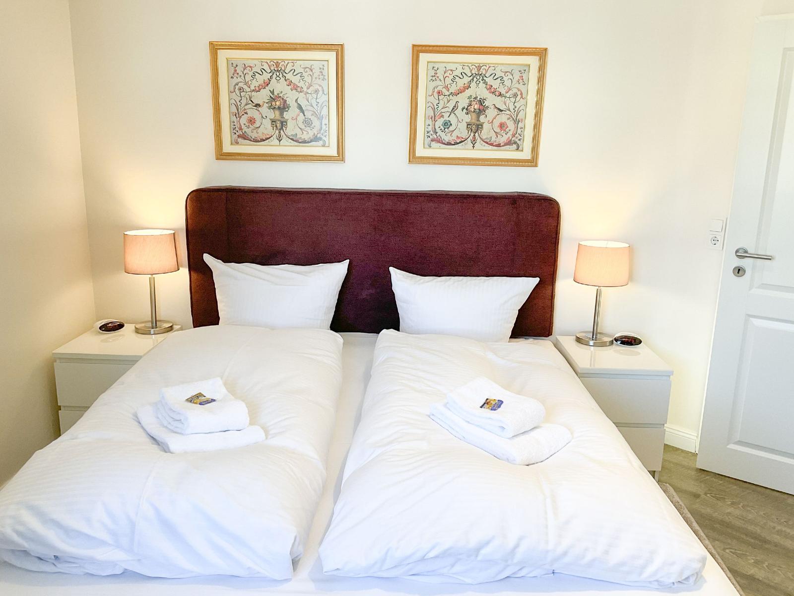 Doppelbett mit weißer Bettwäsche, zwei Nachttische mit Lampen und Bildern an der Wand.