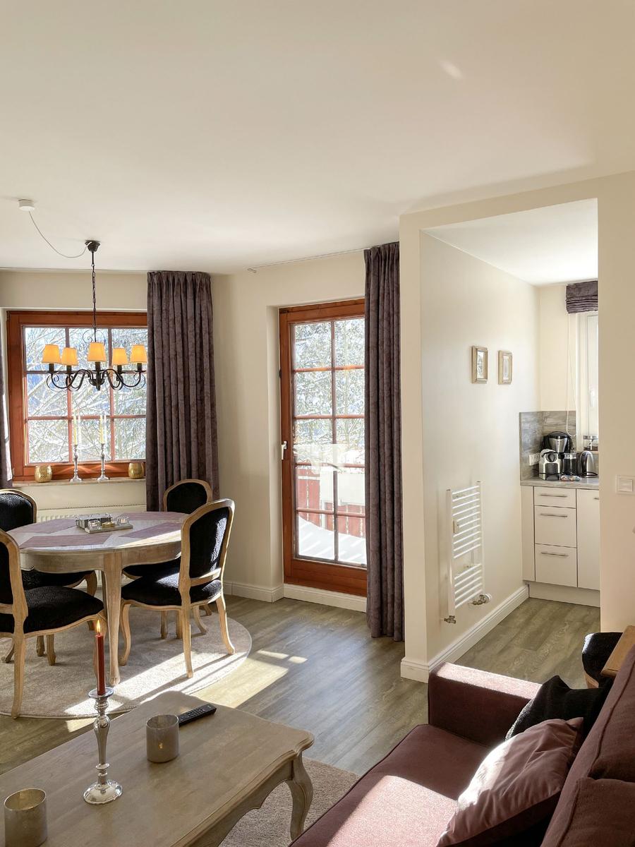 Wohn- und Essbereich mit Tisch, Stühlen und Fensterblick. Küche im Hintergrund.