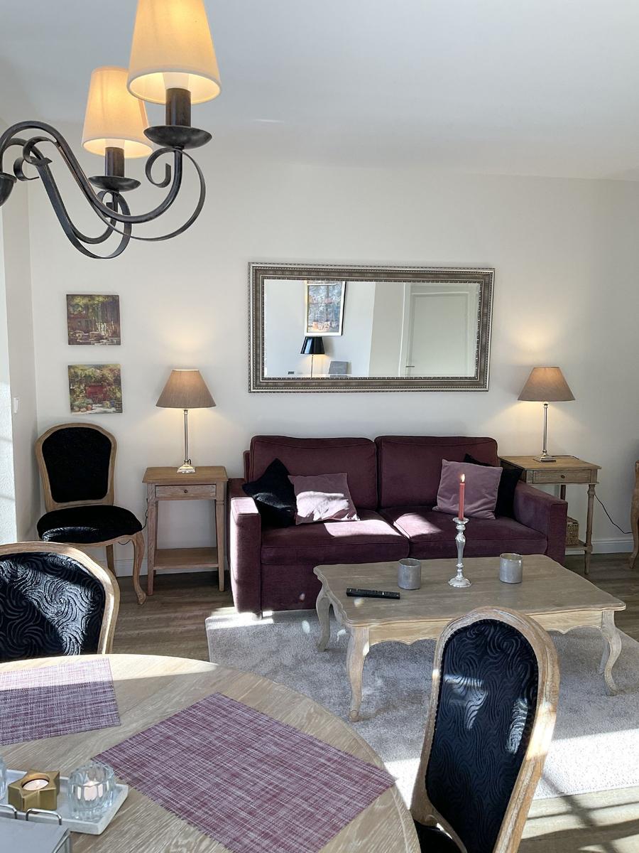 Wohnzimmer mit Sofa, Couchtisch und Stühlen. Hängelampe und Wandspiegel sichtbar.