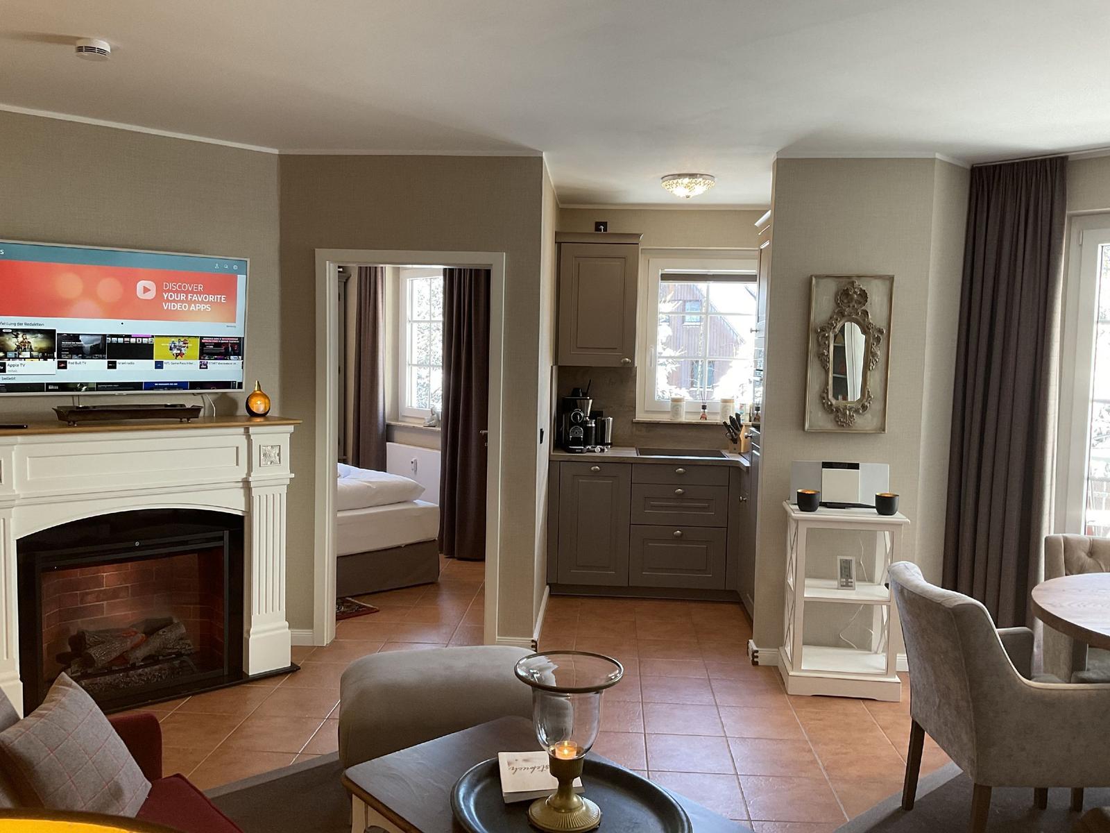 Wohnbereich mit Küche, Fernseher und Kamin. Blick in Schlafzimmer.