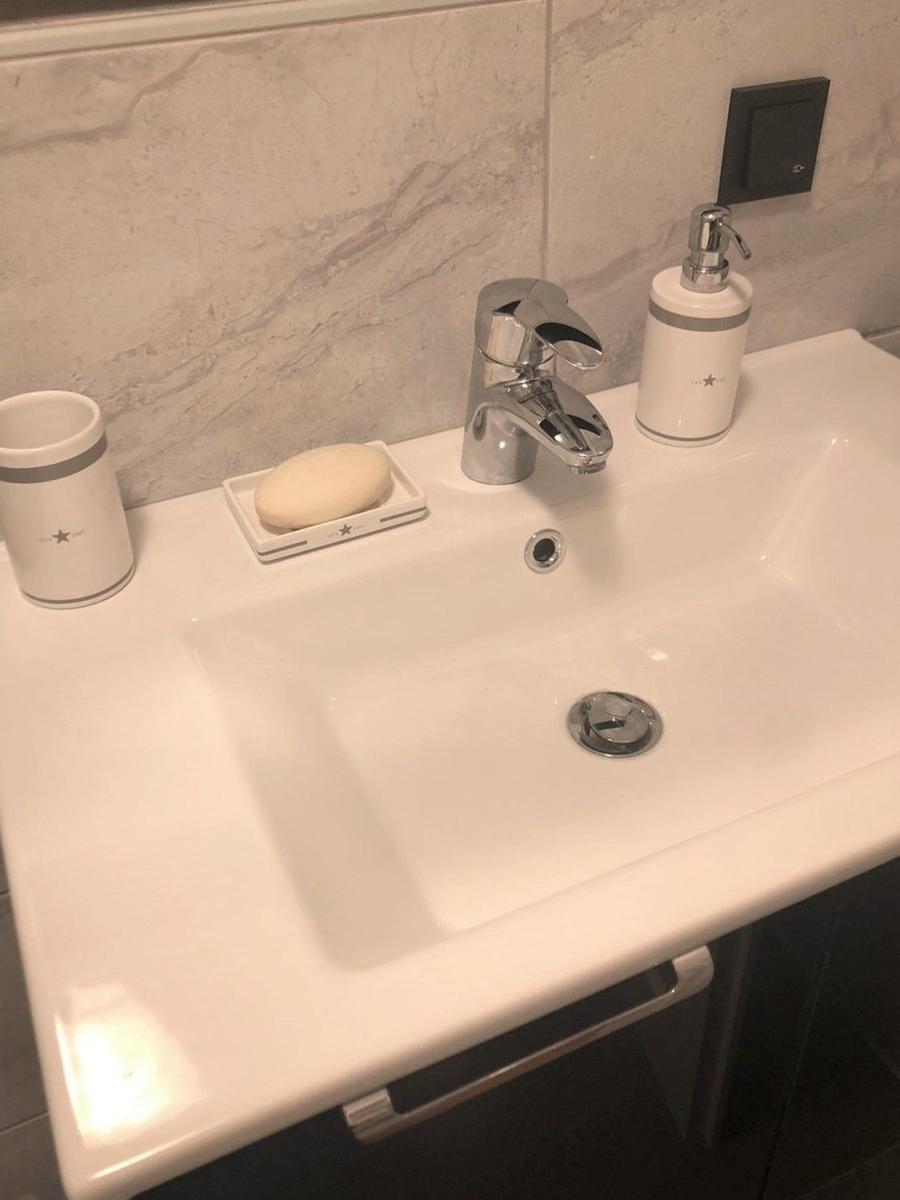 Waschbecken mit Wasserhahn, Seife und Flaschenhalter auf Marmorwand.