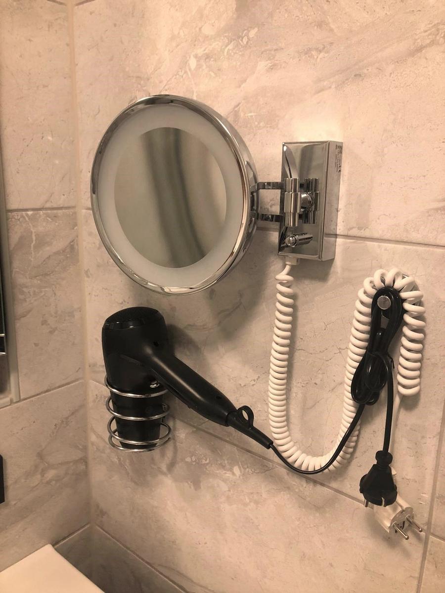 Wandmontierte Haartrockner- und Spiegelanlage mit Lichtumrandung und Steckeranschluss.