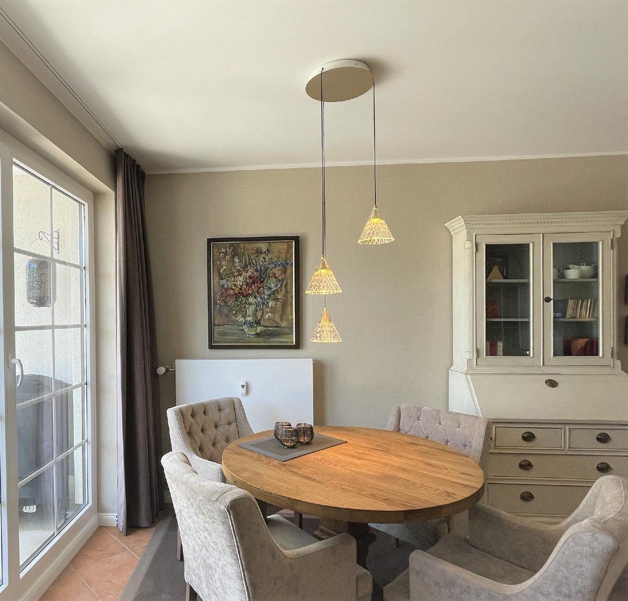 Esszimmer mit runden Tisch, vier Stühlen und weißen Schränken. An der Wand hängt ein Bild.