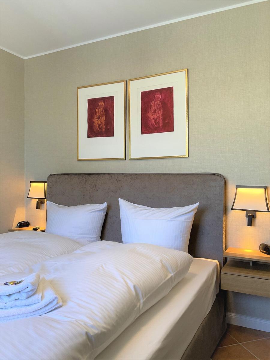 Schlafzimmer mit Bett, zwei Nachttischen und zwei Wandbildern über dem Kopfteil.