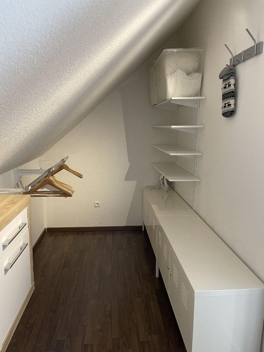 Dachbodenraum mit Schrank, Kleiderhaken und Regalen. Holzfußboden und schräges Dach.