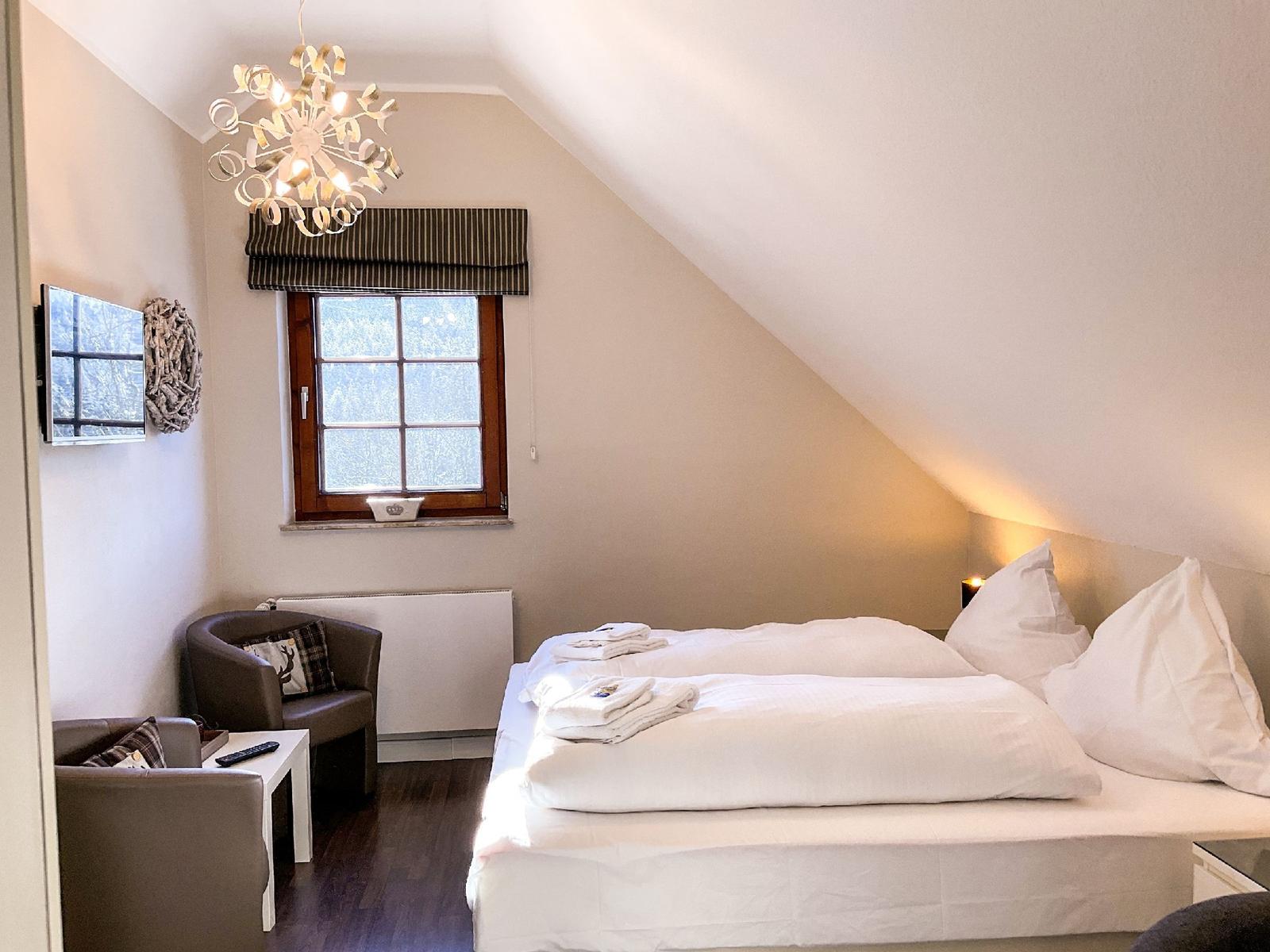 Schlafzimmer mit Dachschrägen, Bett, Fenster und Sitzgelegenheit.