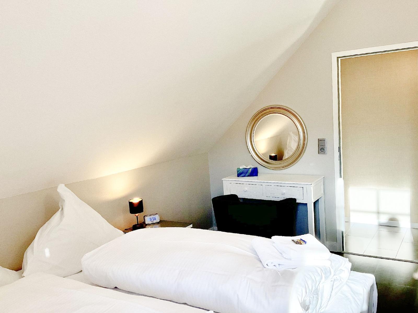 Schlafzimmer mit Dachschräge, Bett, Schreibtisch und Spiegel.