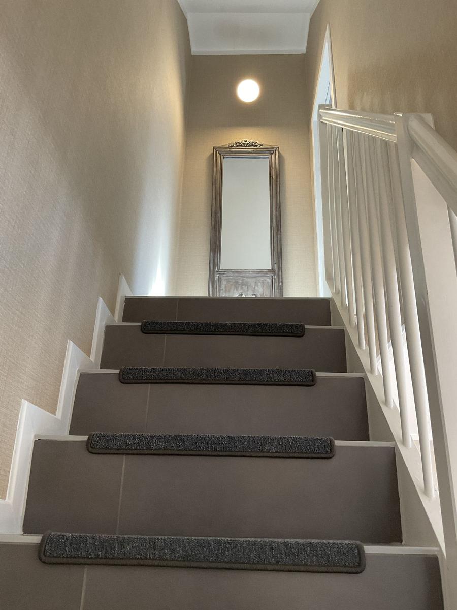 Treppenhaus mit grauer Treppe und weißem Geländer. Spiegel und Deckenleuchte sind sichtbar.