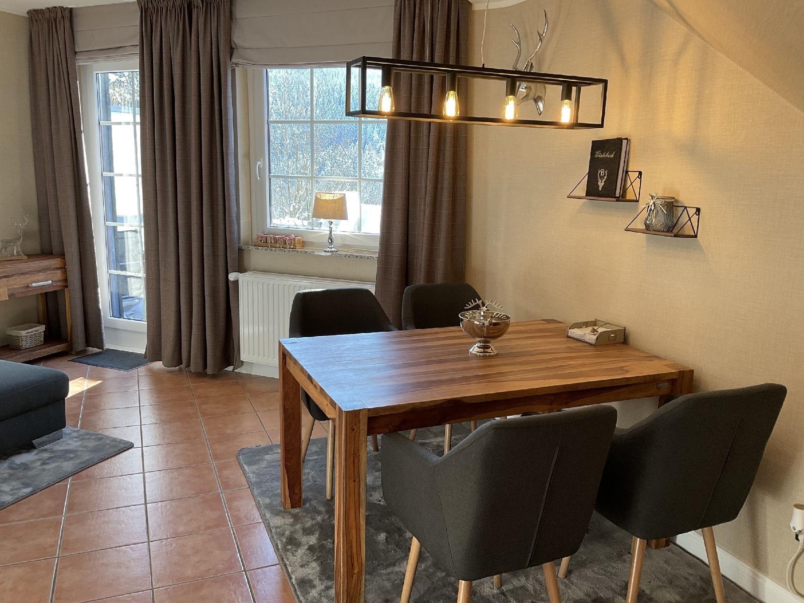 Esstisch mit vier Stühlen, Wandregale und Fenster mit Vorhängen.