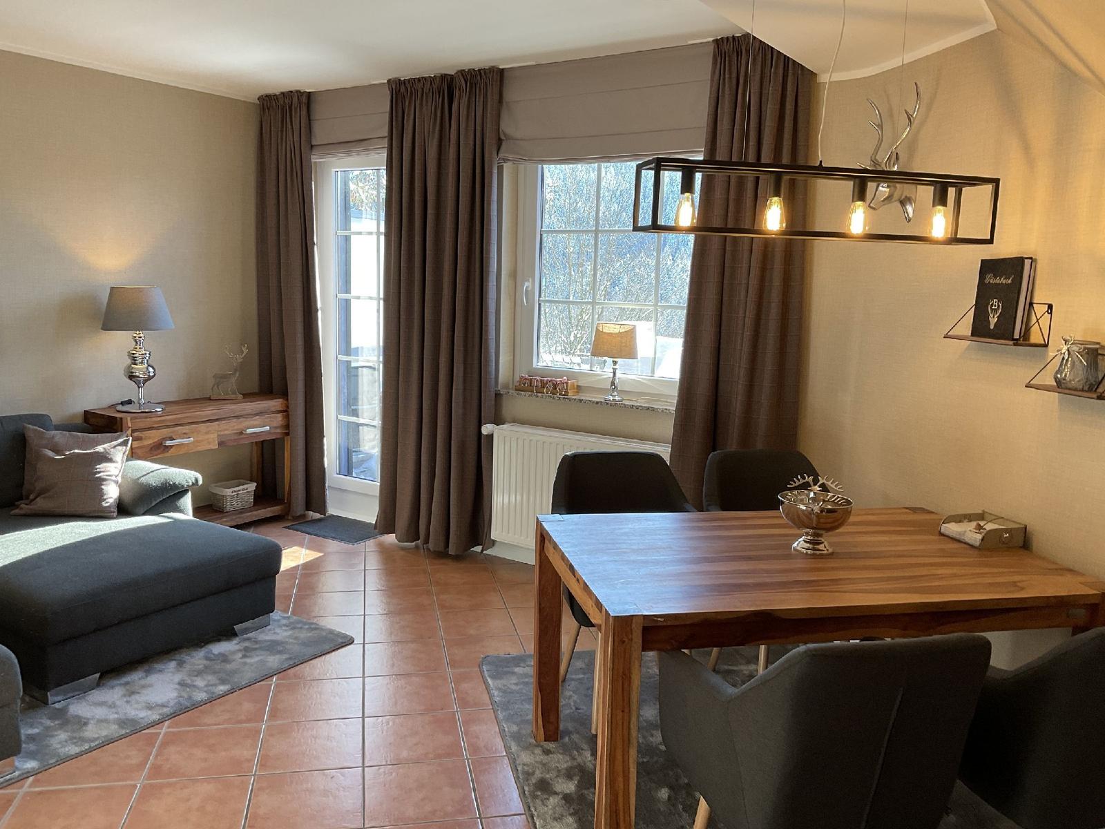 Ein Esszimmer mit Holztisch und Stühlen, daneben ein Wohnbereich mit Sofa und Fenster.