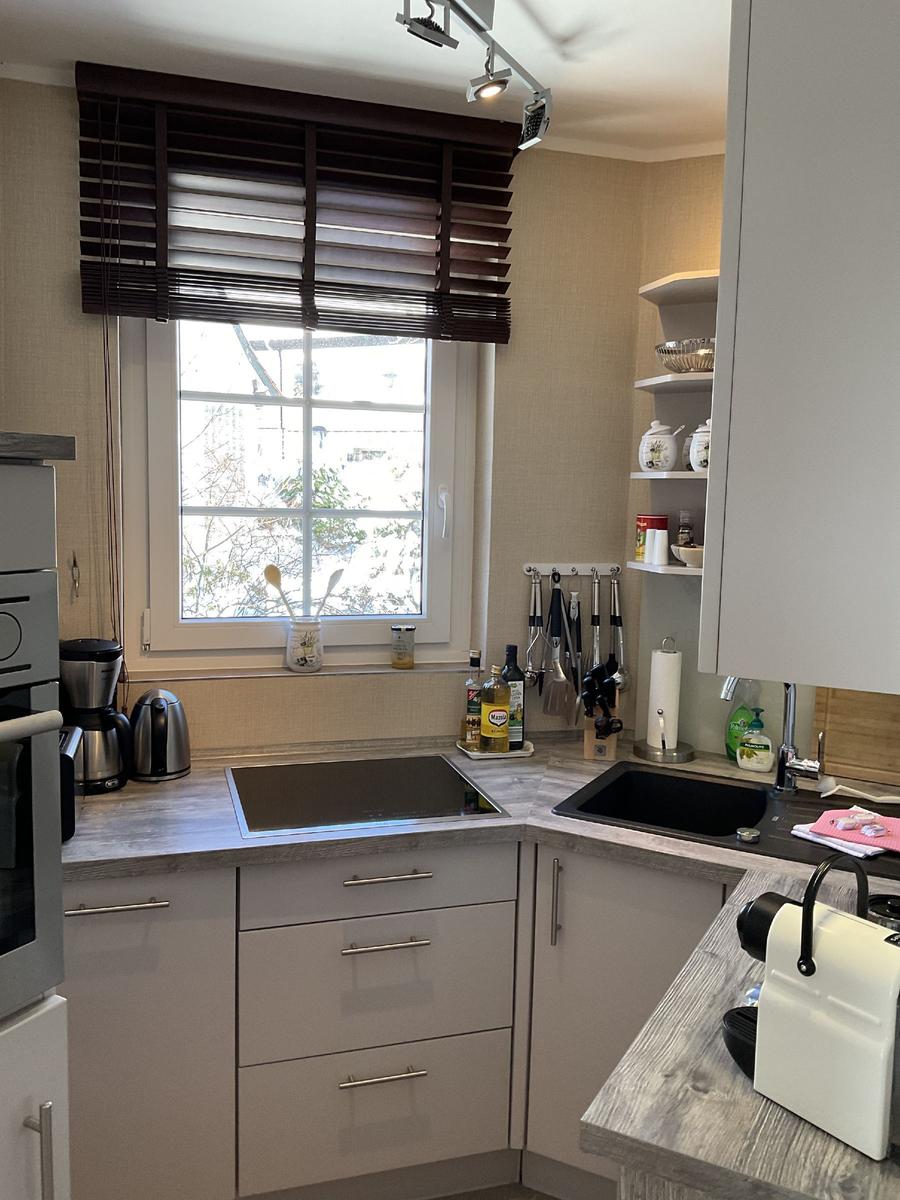 Küche mit Arbeitsfläche, Spüle und Fenster mit Jalousie.
