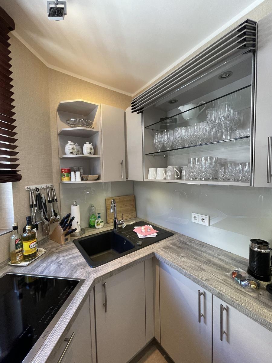 Küche mit Arbeitsplatte, Spüle und Glasregal mit Geschirr.