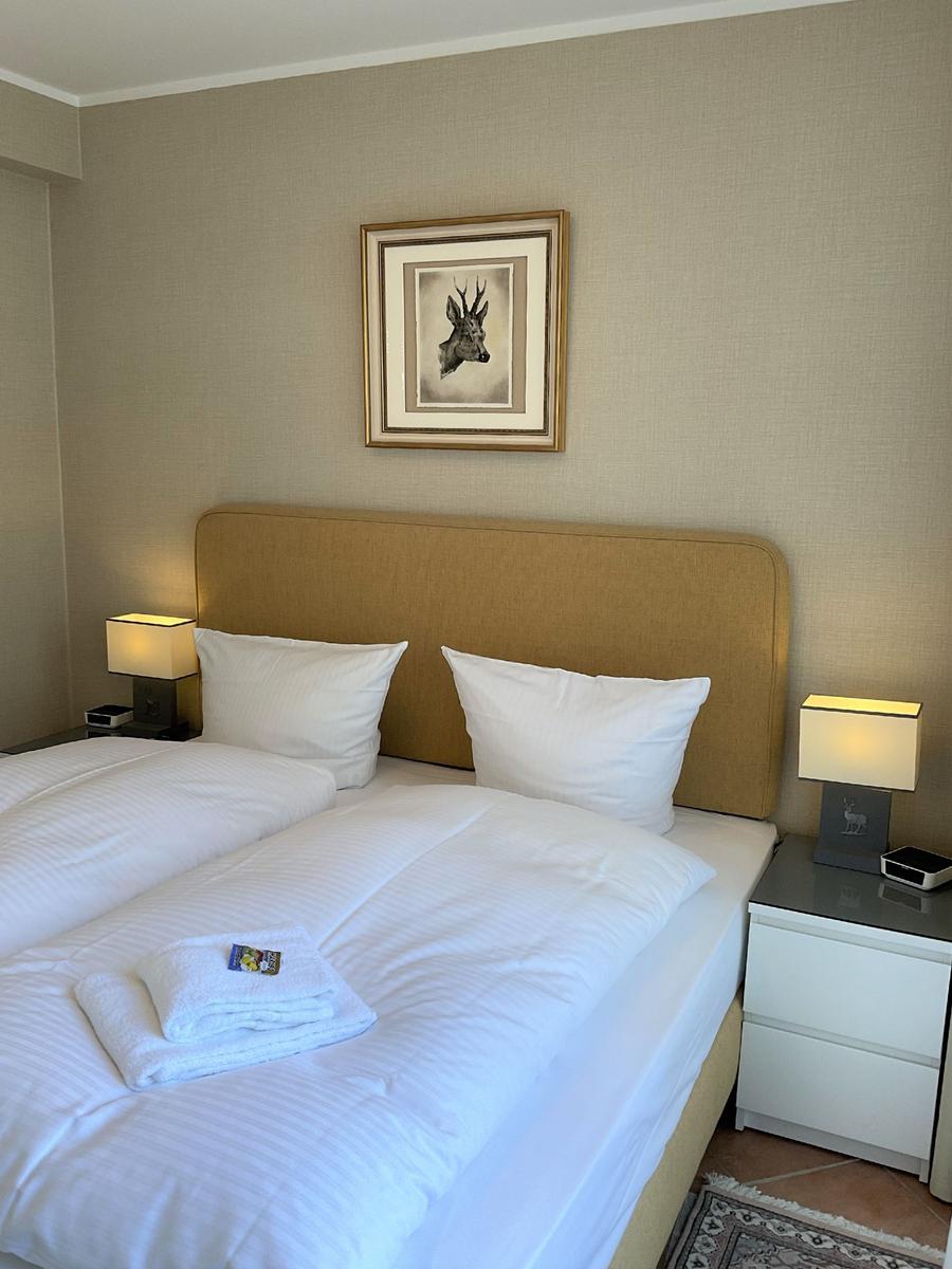 Doppelbett mit weißer Bettwäsche, zwei Nachttische mit Lampen und Bild an der Wand.