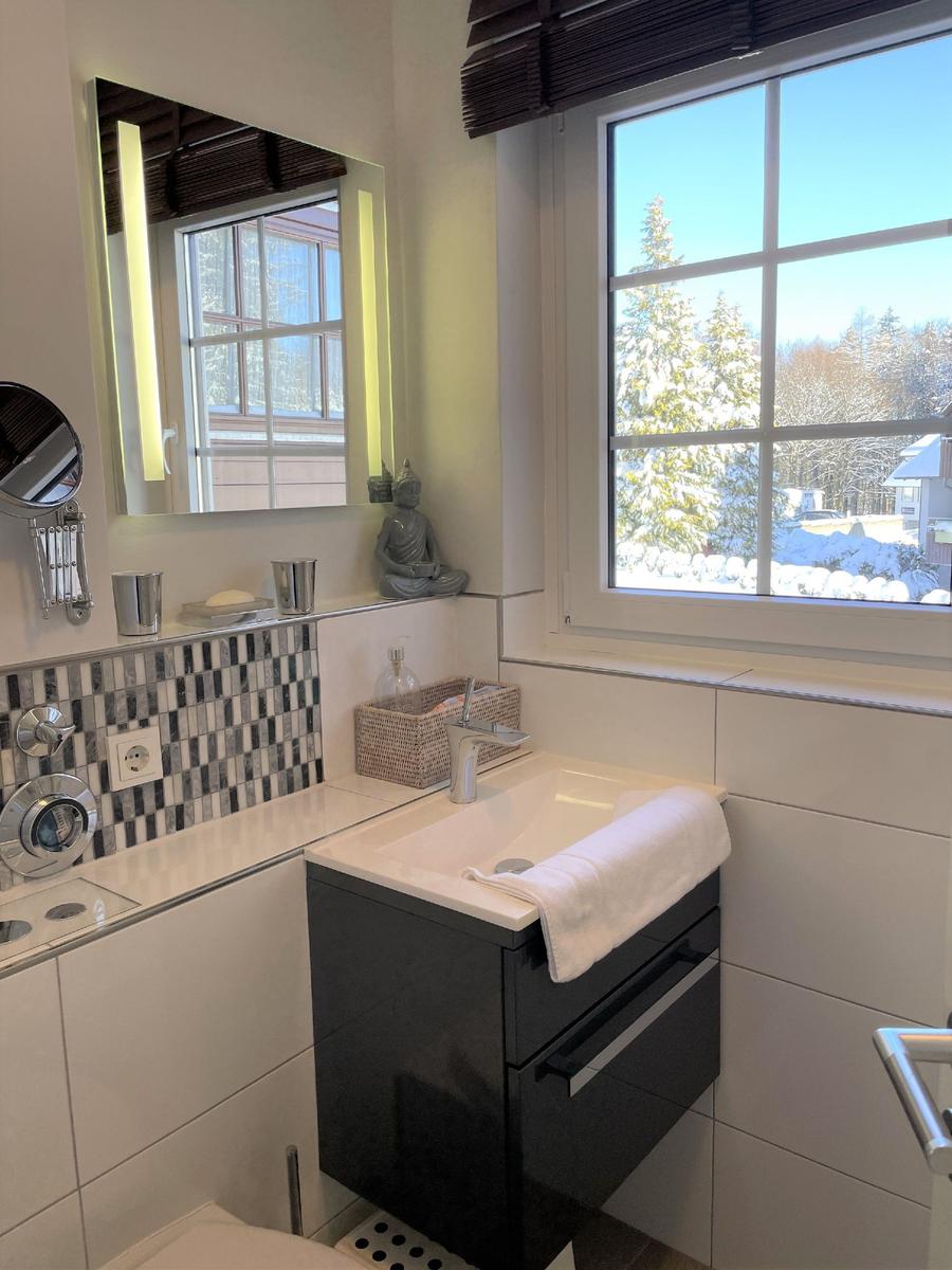 Badezimmer mit Waschbecken, Spiegel und Fensterblick auf Schnee.