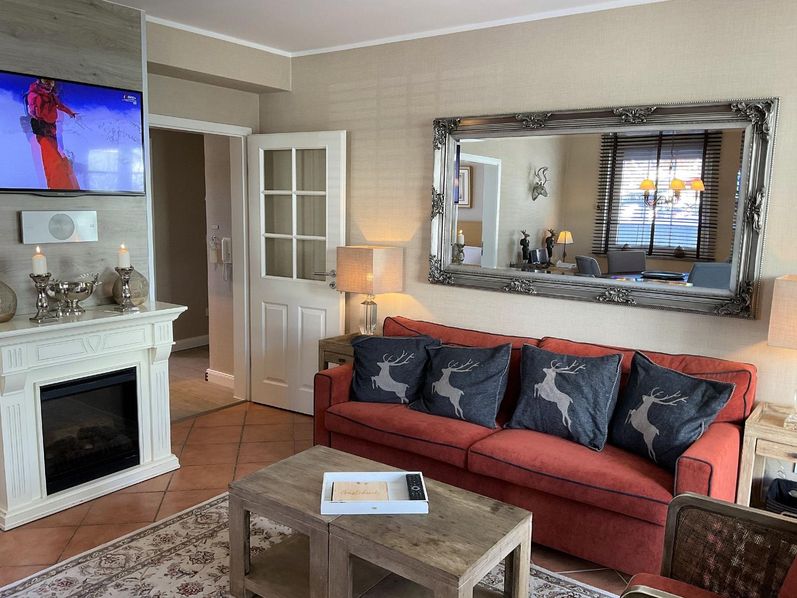 Ein Wohnzimmer mit rotem Sofa, Kamin und Fernseher. An der Wand hängt ein großer Spiegel.