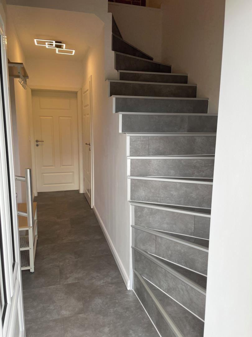 Haus mit Treppe und Flur mit weißen Türen und grauem Bodenbelag.