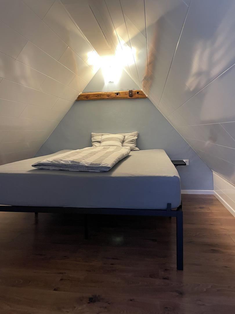 Schlafzimmer mit Dachschräge, Bett und Holzboden.