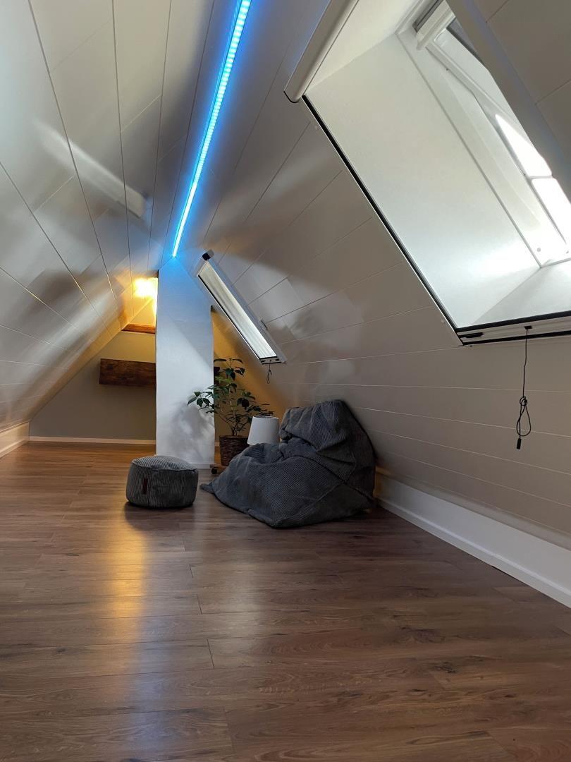 Dachgeschosszimmer mit Holzboden, Dachschrägen und großen Fenstern.
