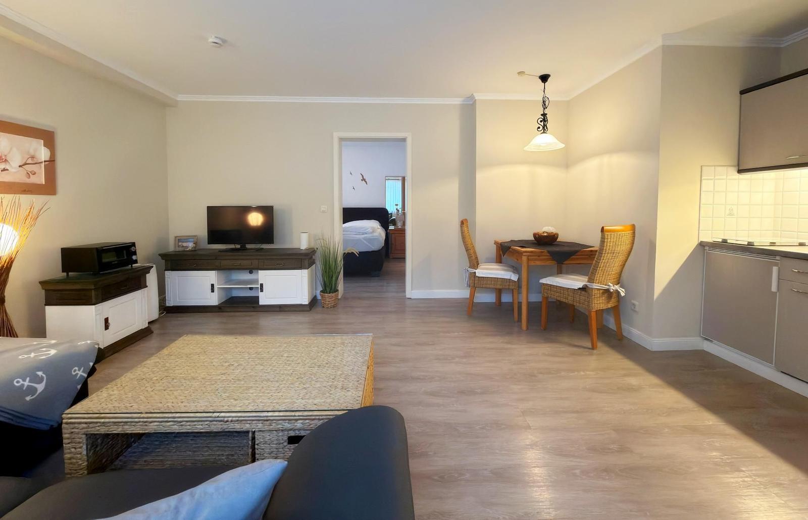 Wohnzimmer mit Essbereich und Küche. Fernseher, Tisch, Stühle und Schlafzimmer im Hintergrund.