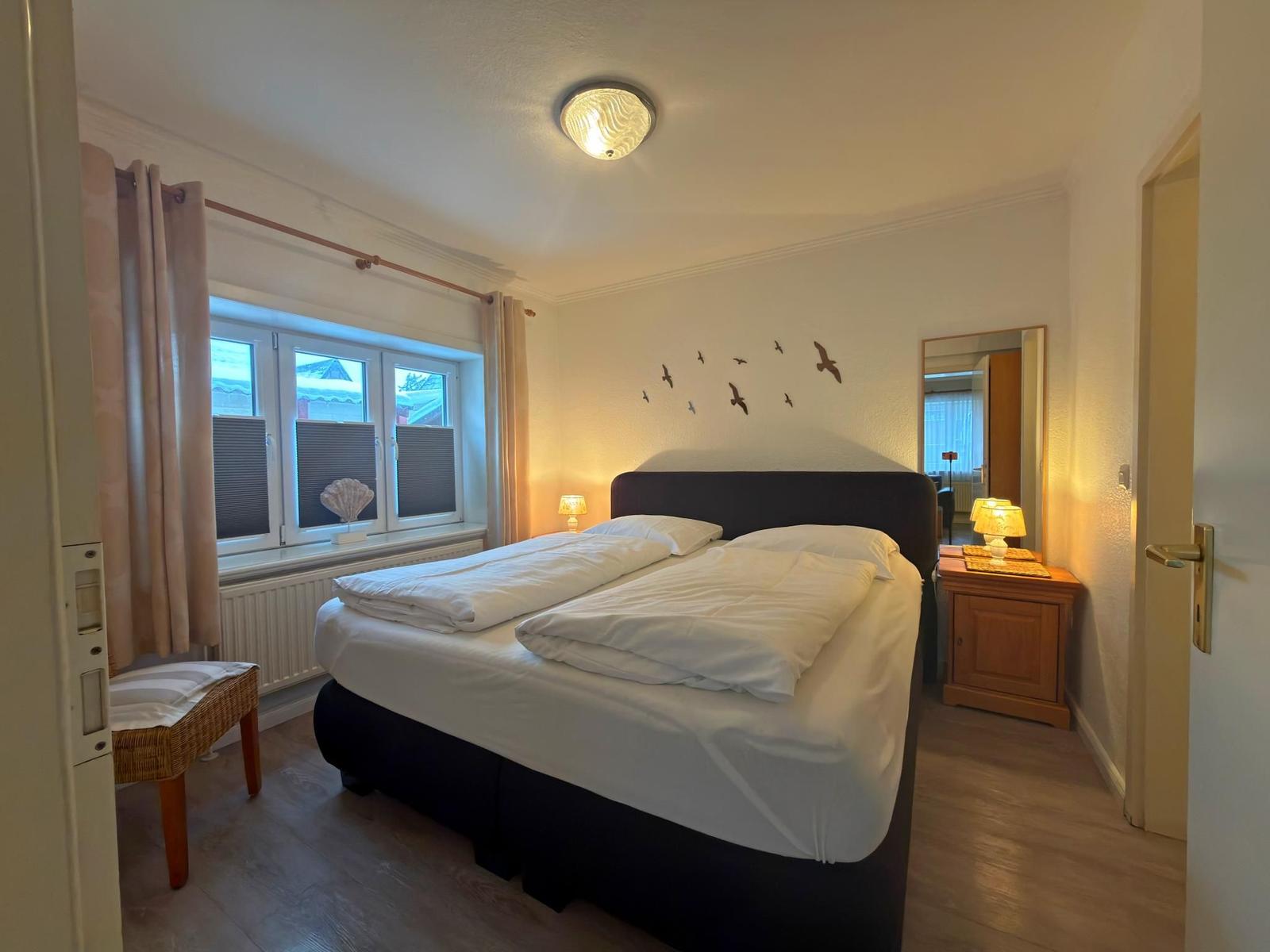 Schlafzimmer mit Doppelbett, Fenster, Nachttisch und Wanddekoration.