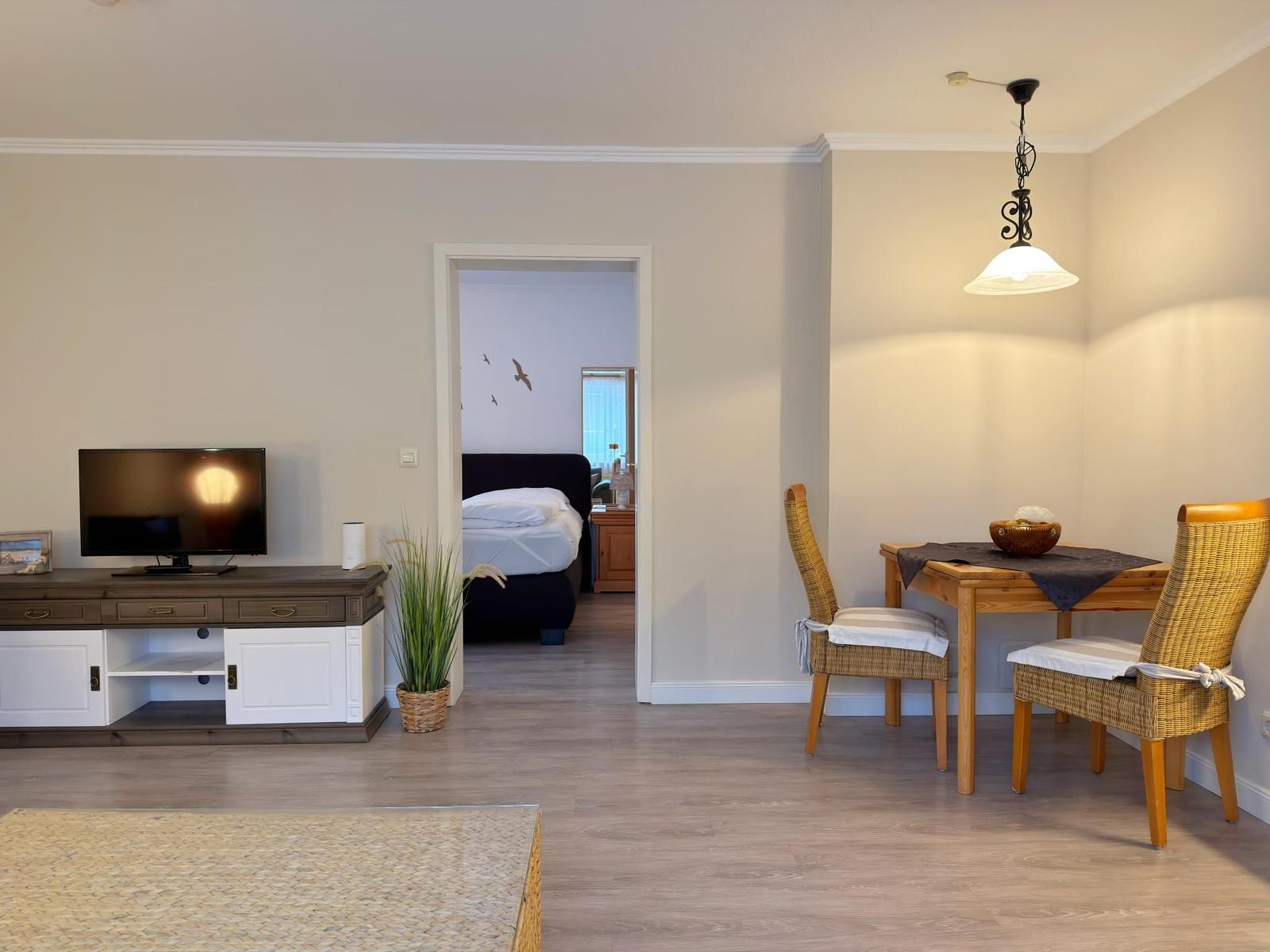 Wohnbereich mit Essplatz, TV und Blick in Schlafzimmer mit Bett.