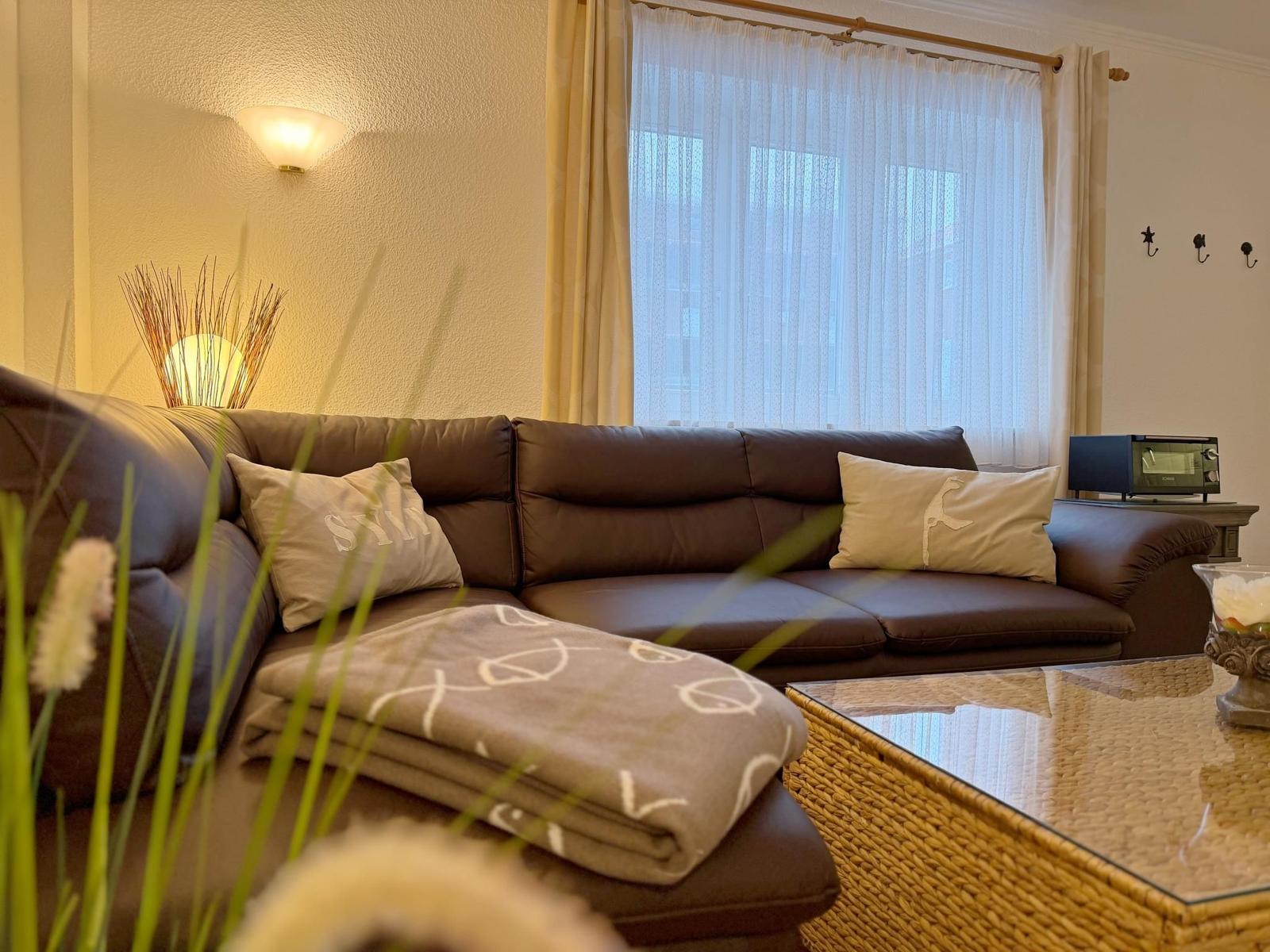 Ein Wohnzimmer mit braunem Sofa, dekorativen Kissen und einem Glas-Tisch.