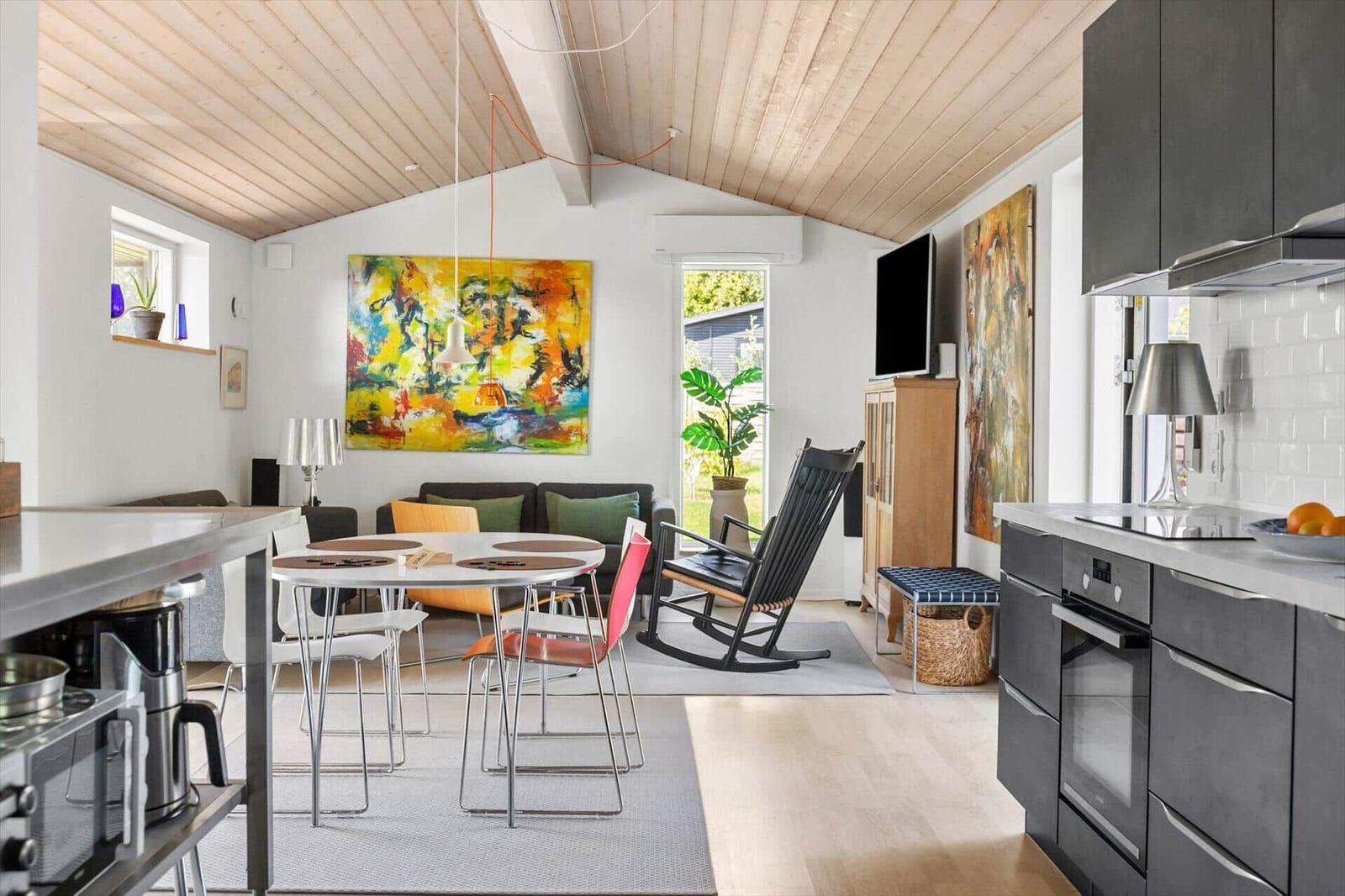 Kitchen with dining area and living room under wooden ceiling. Large wall art and plants.