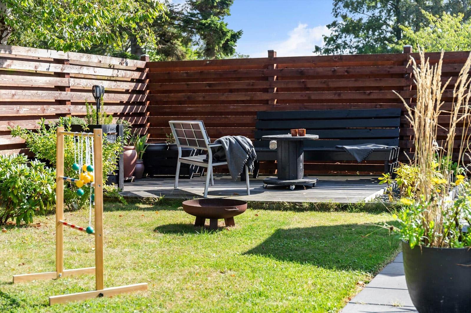 Backyard with wooden deck, seating, and lawn game on grass.