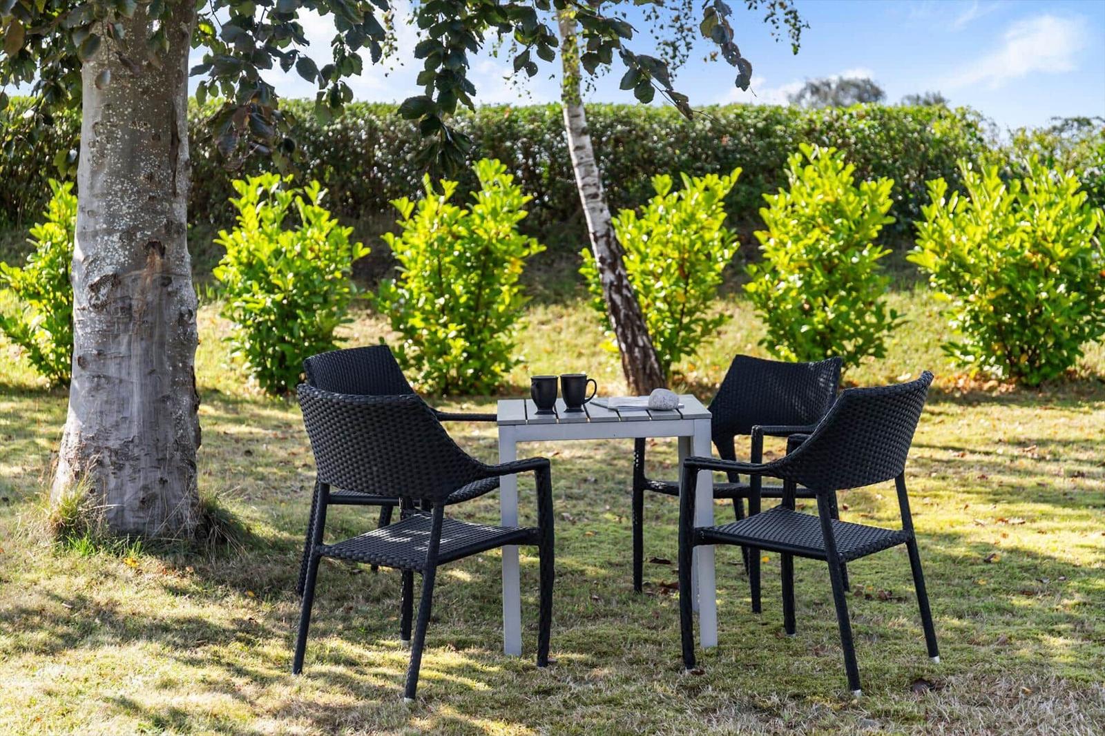 Outdoor area with table and four chairs under trees on grass.