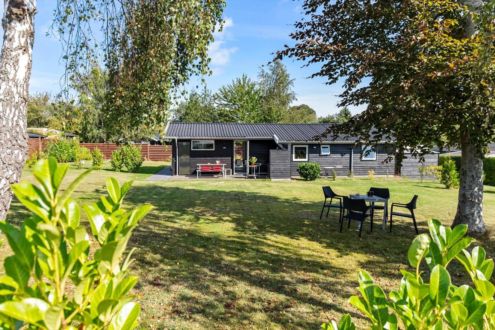 A dark holiday house with garden, terrace, and seating areas under trees.