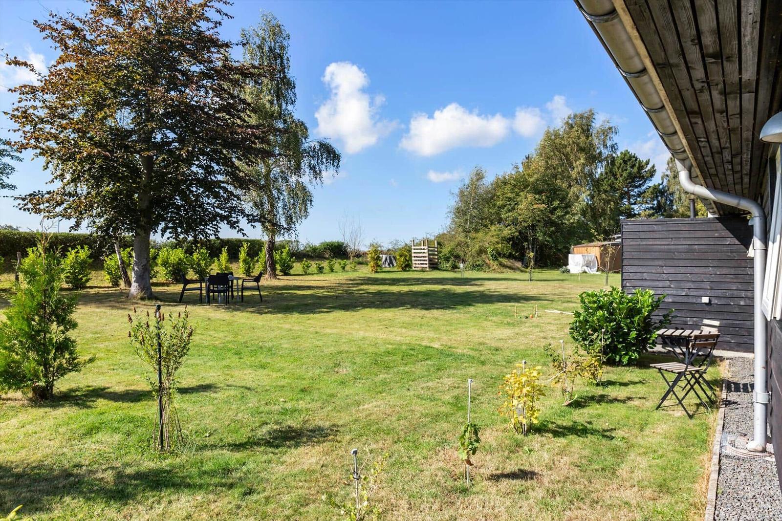 Large garden with seating areas and trees under a blue sky.