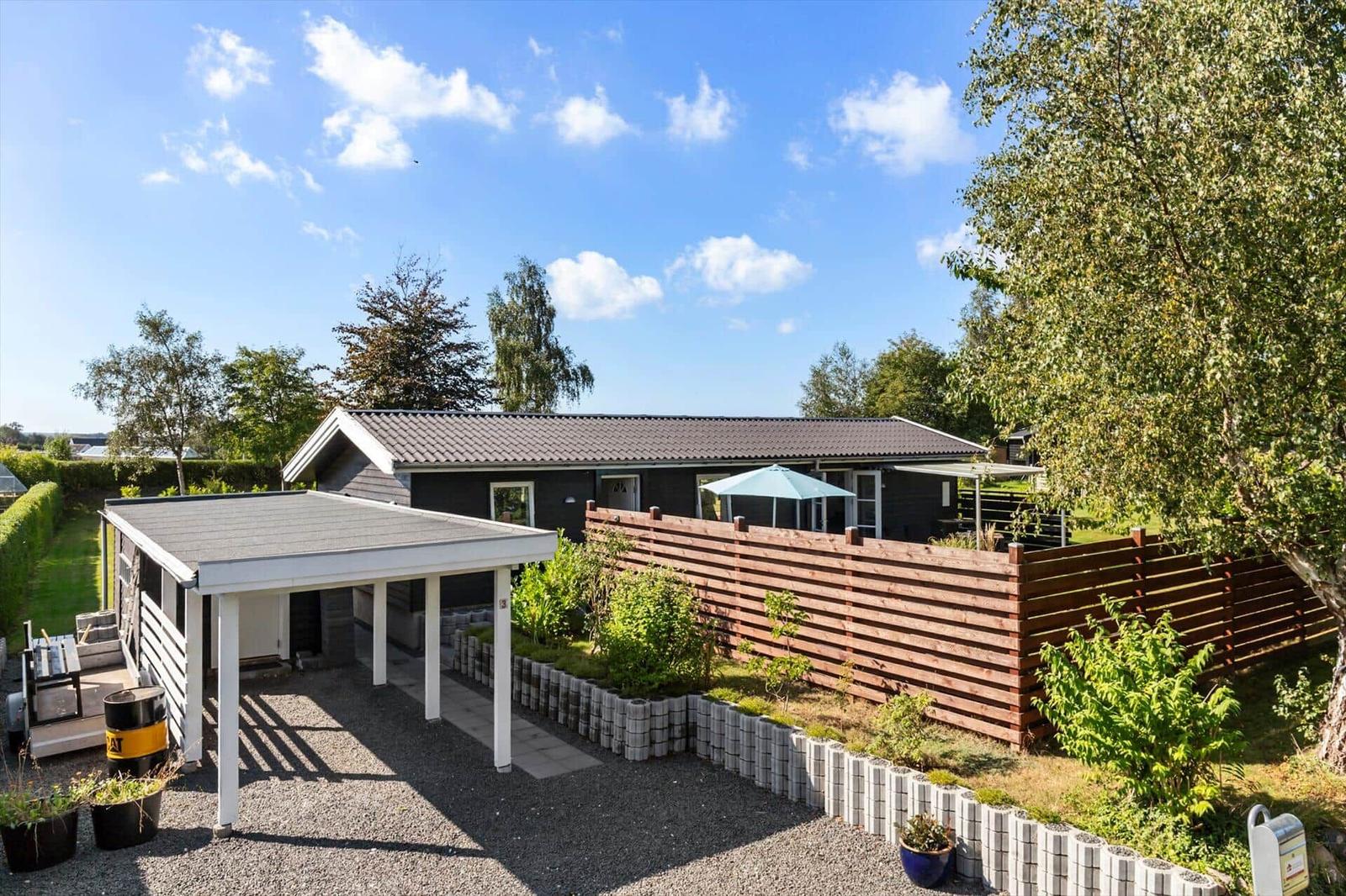 A modern house with terrace, wooden fence, and garden area under blue sky.