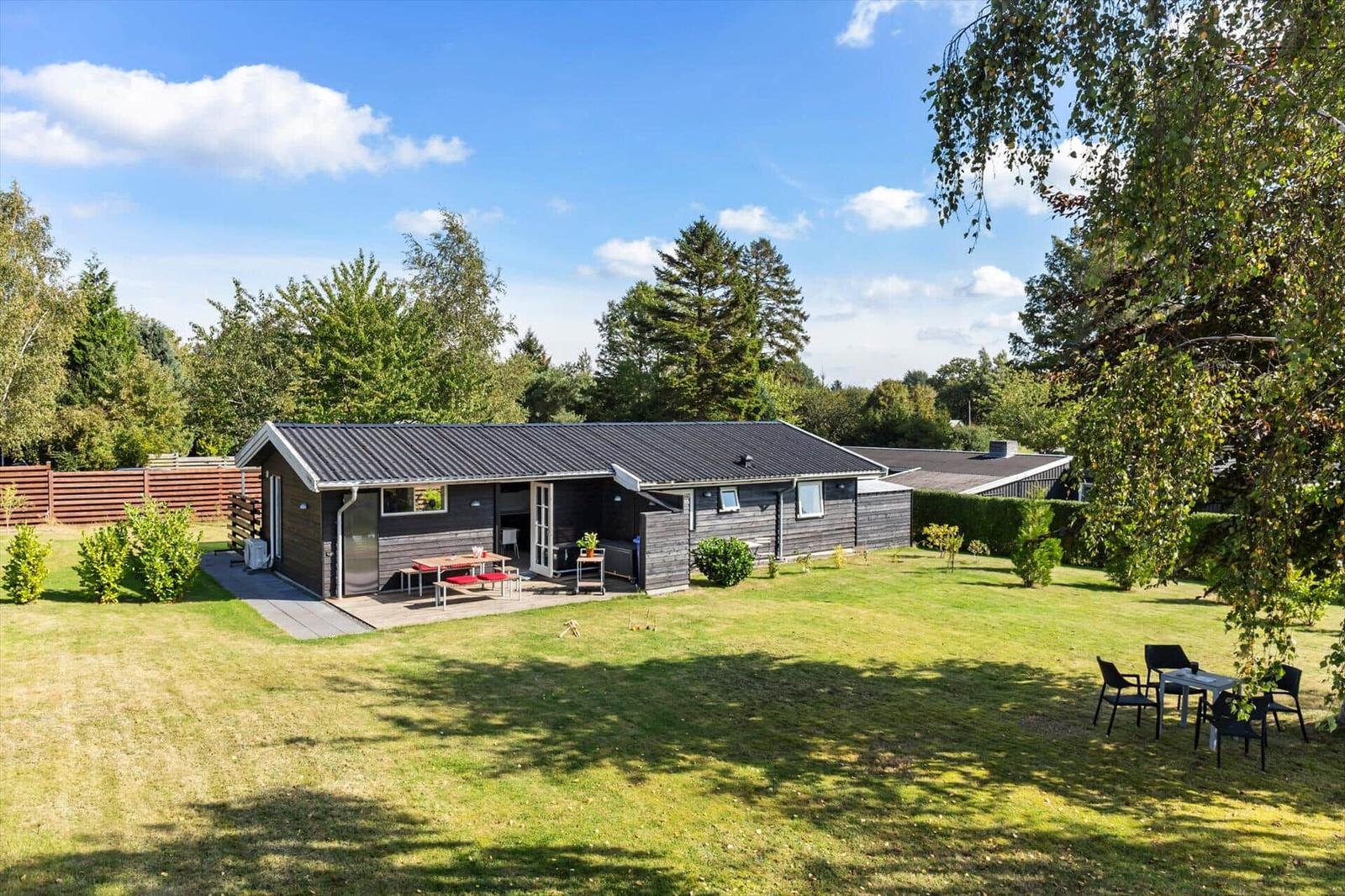 A house with terrace, garden, and seating areas under trees.