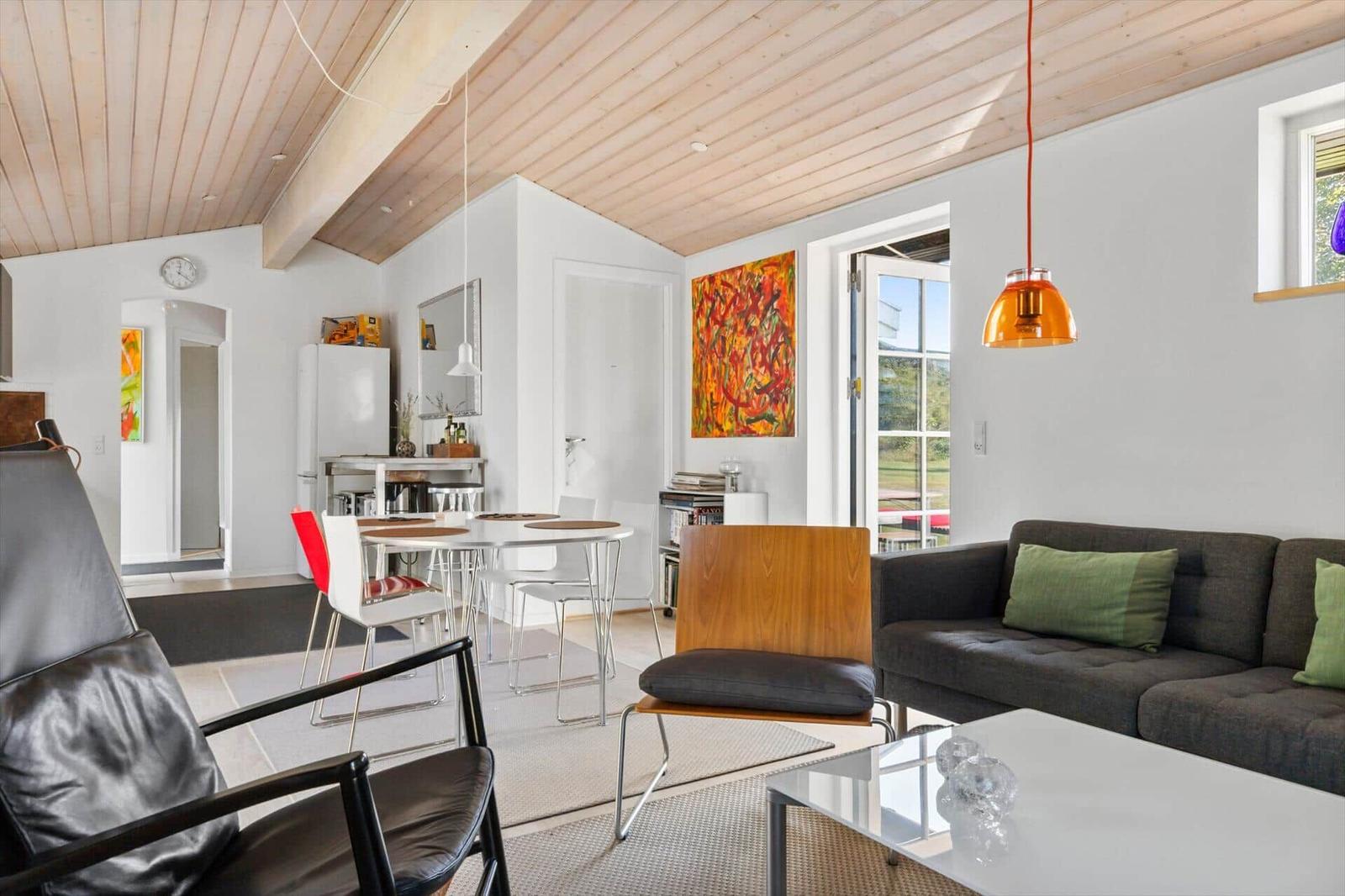 Living and dining area with sofa, table and chairs under wooden ceiling.