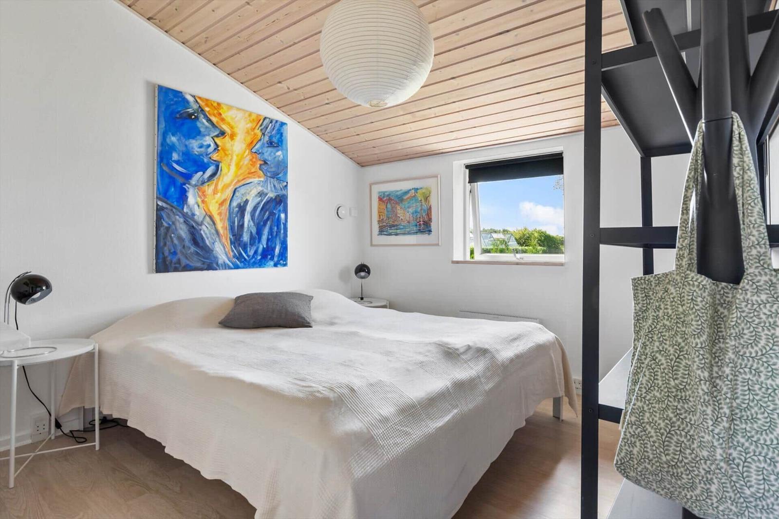 Bedroom with bed, wall art, and window with view of greenery.