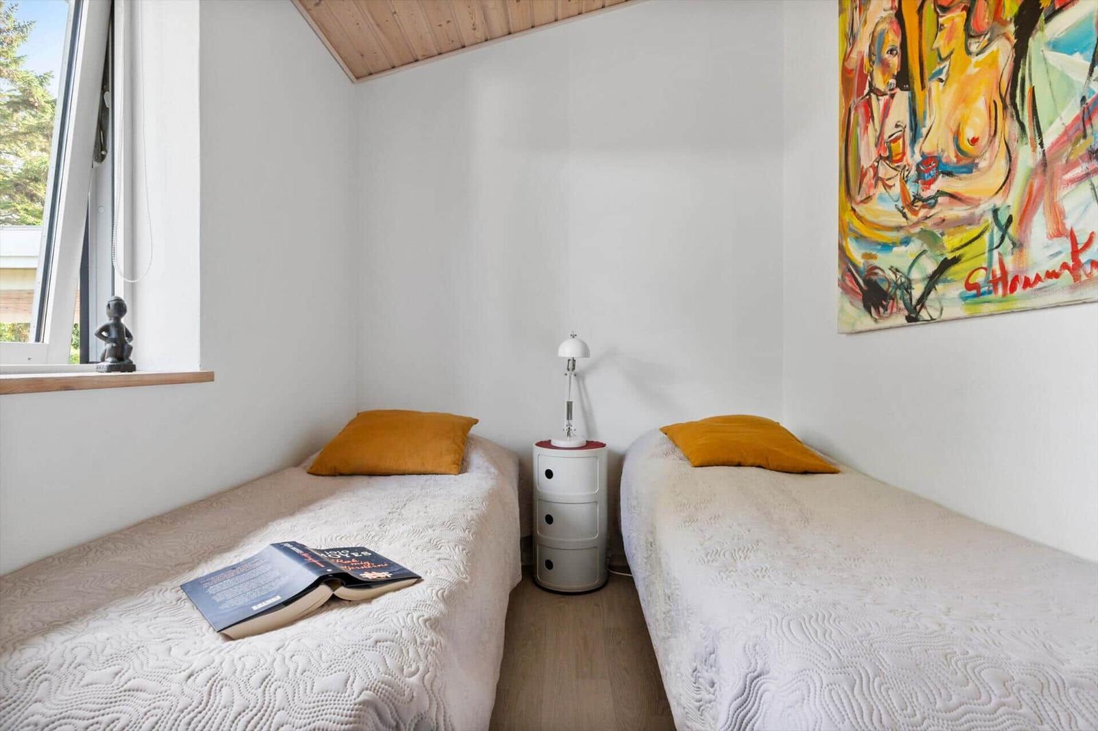 Two beds with yellow pillows, nightstand, and wall art. Window with view outside.