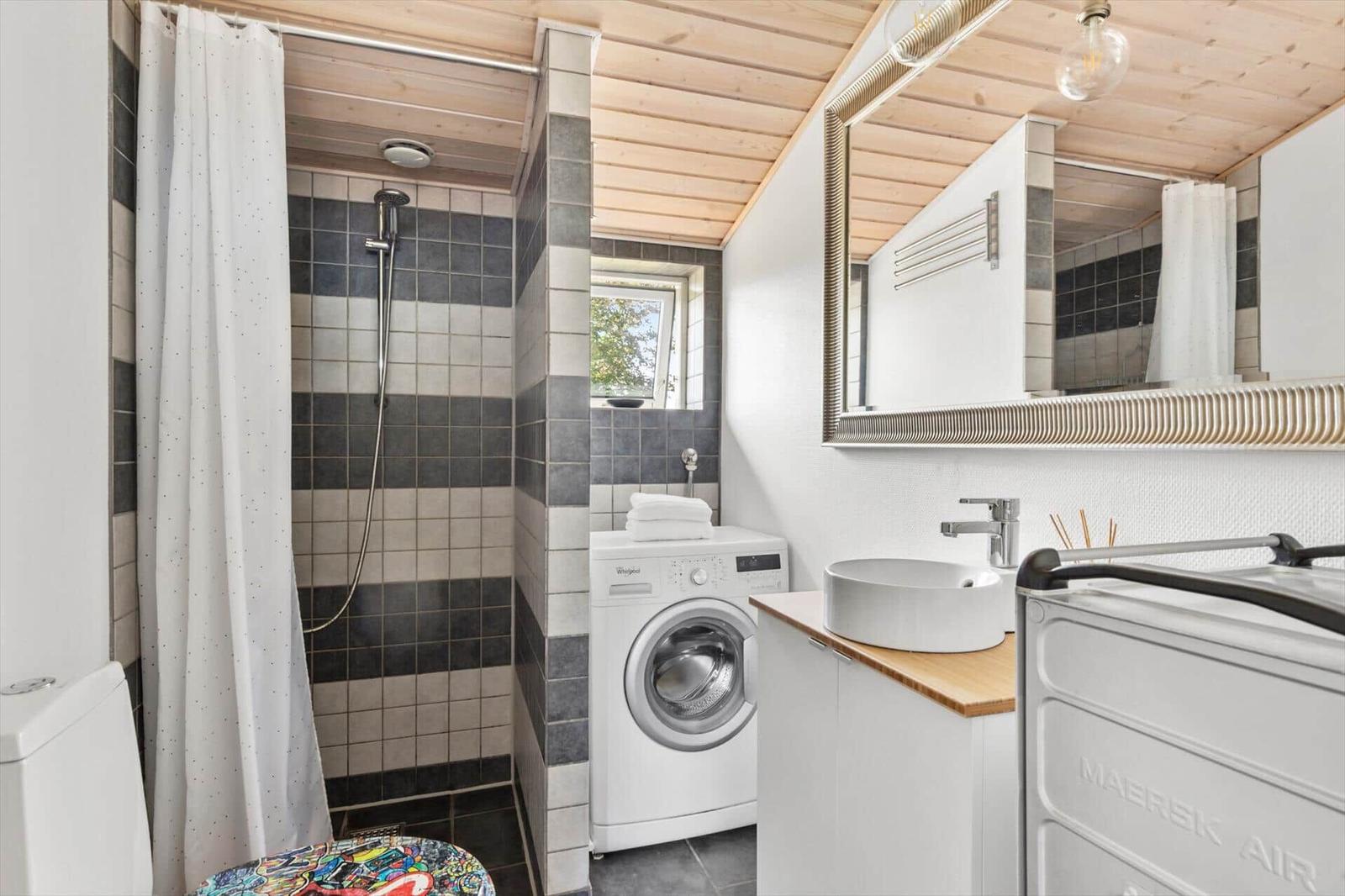 Bathroom with shower, washing machine, and sink. Wooden ceiling and window.
