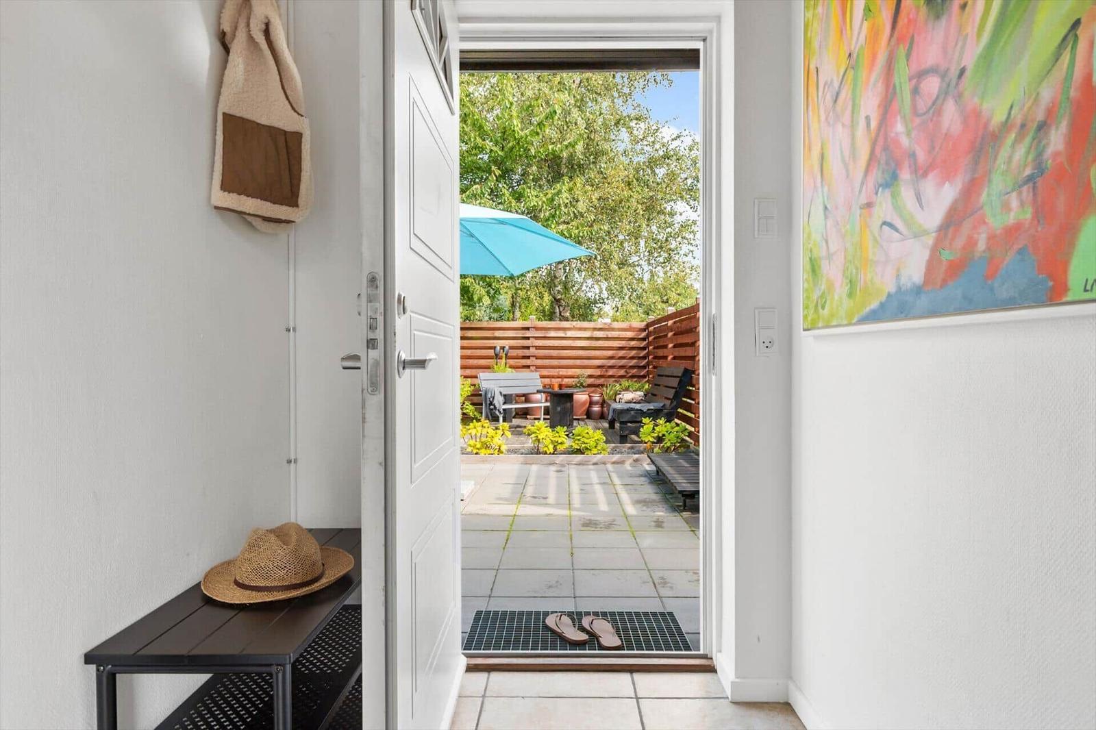 Through the door, a garden with table, chairs, and blue umbrella is visible.