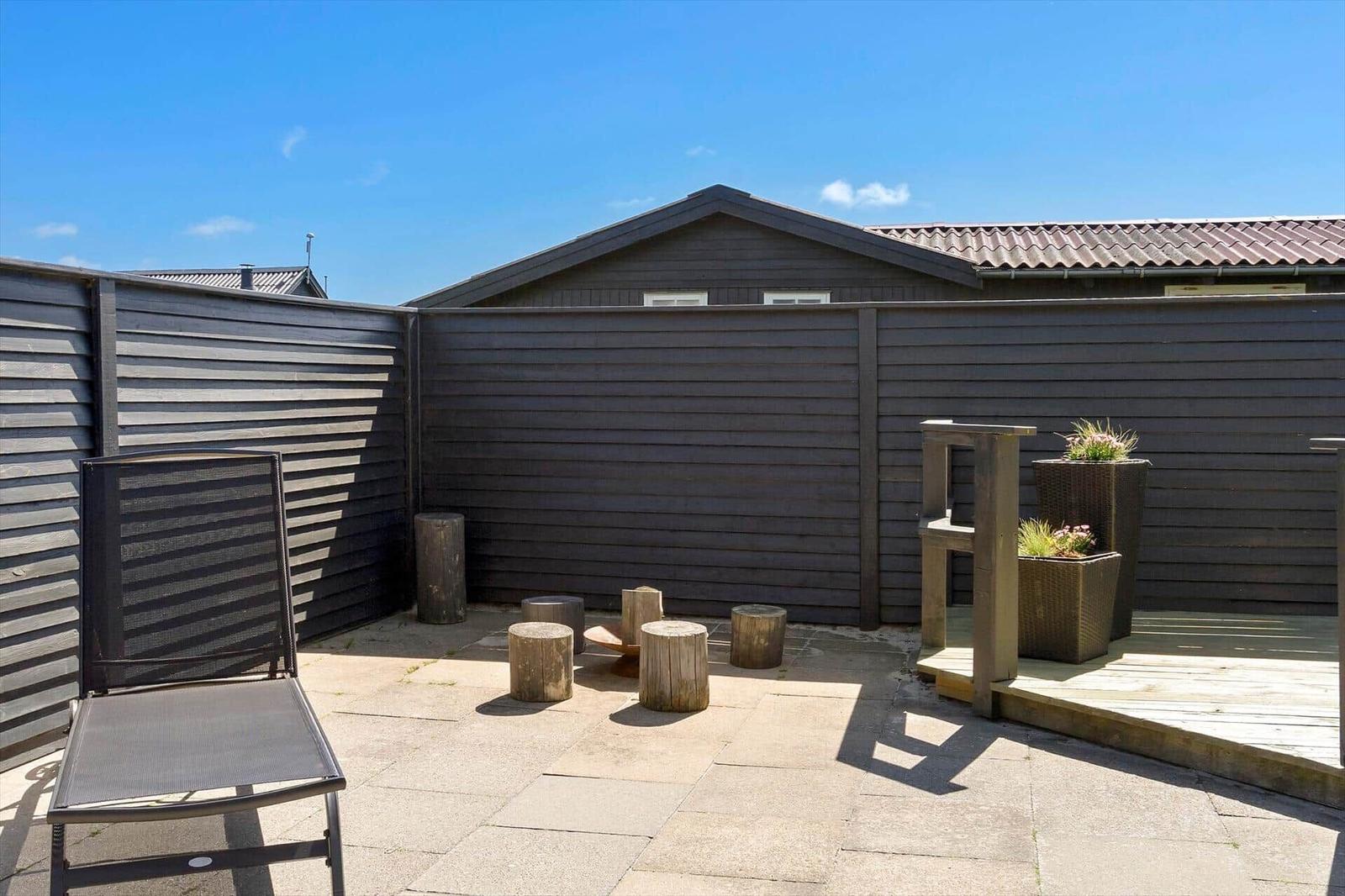 Terrace with sun lounger, wooden stools, and planters. Background: wooden fence and roof.