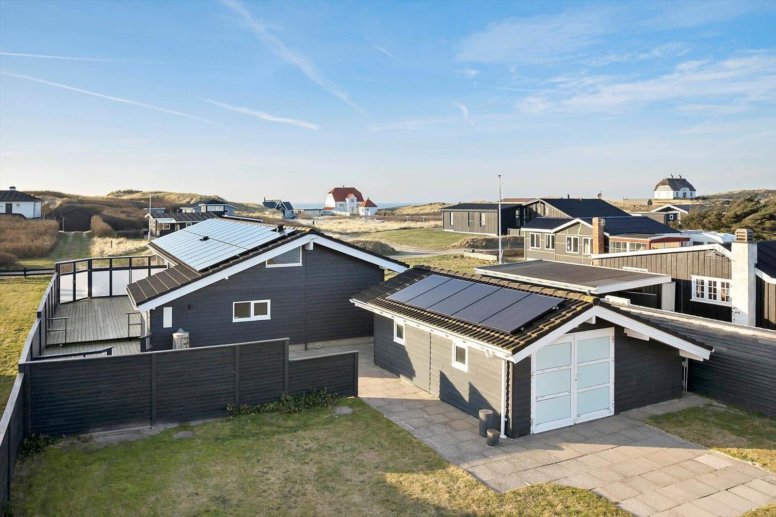 Modern vacation home with solar panels and terrace. View of dunes and holiday homes.