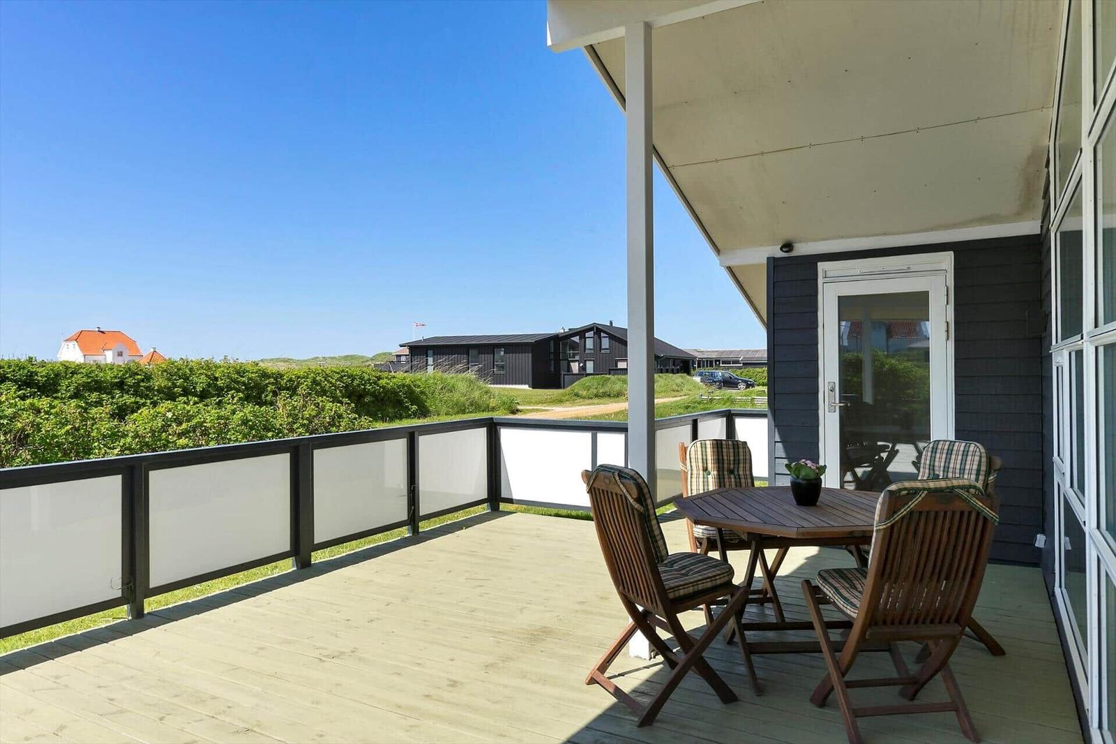 Terrace with table and chairs, view of greenery and houses.