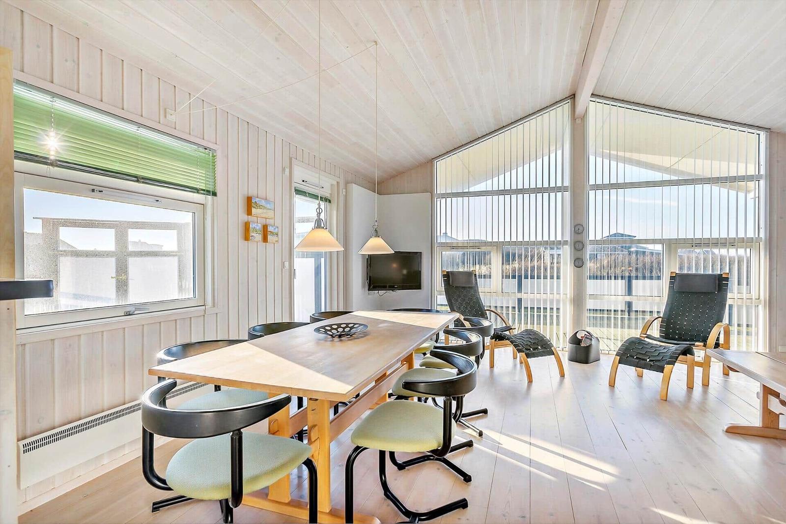 Large room with dining table, chairs, and seating. Large windows and wooden ceiling.