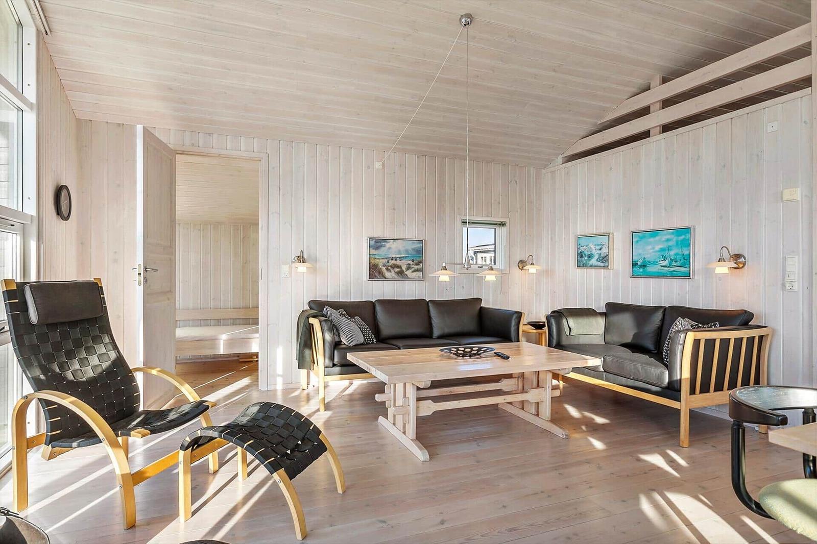 Living room with wooden walls, sofa, table, and chair. Passage to the bedroom.