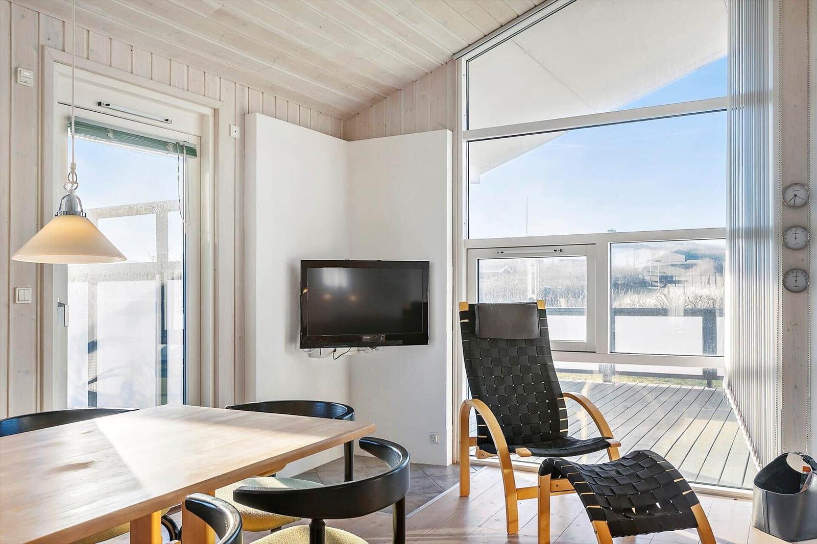 Dining area with table, chairs, and TV. Large windows overlook the terrace.
