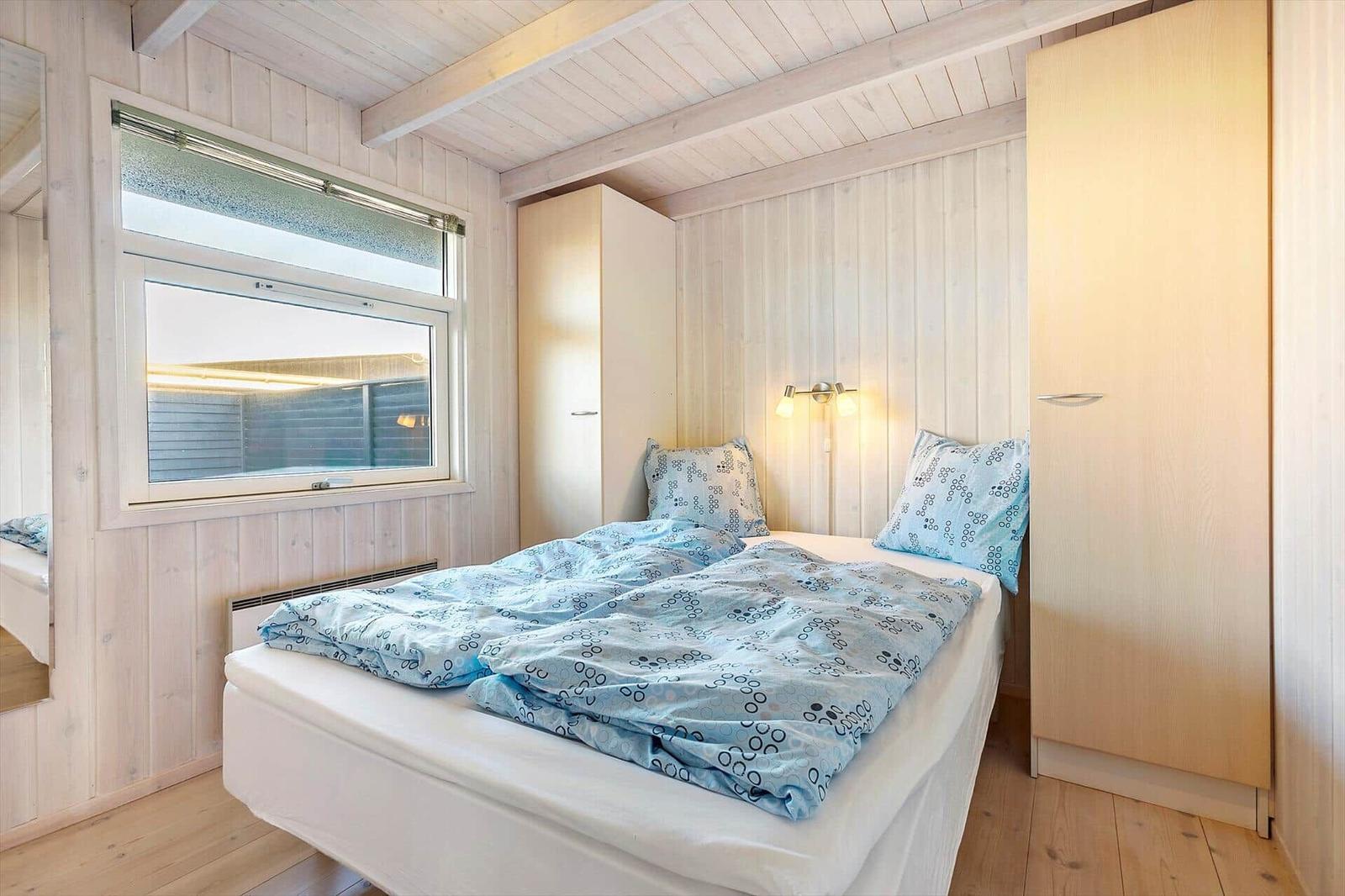 Bedroom with bed, window, and closets. Wooden walls and floor.