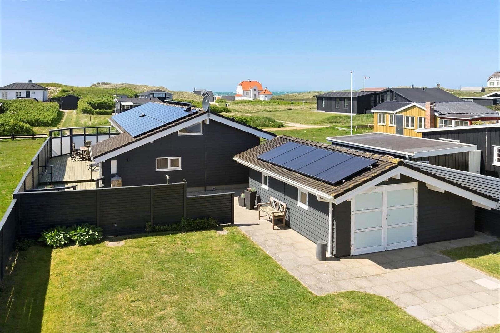 A modern house with solar panels, terrace, and garden. View of the coast.