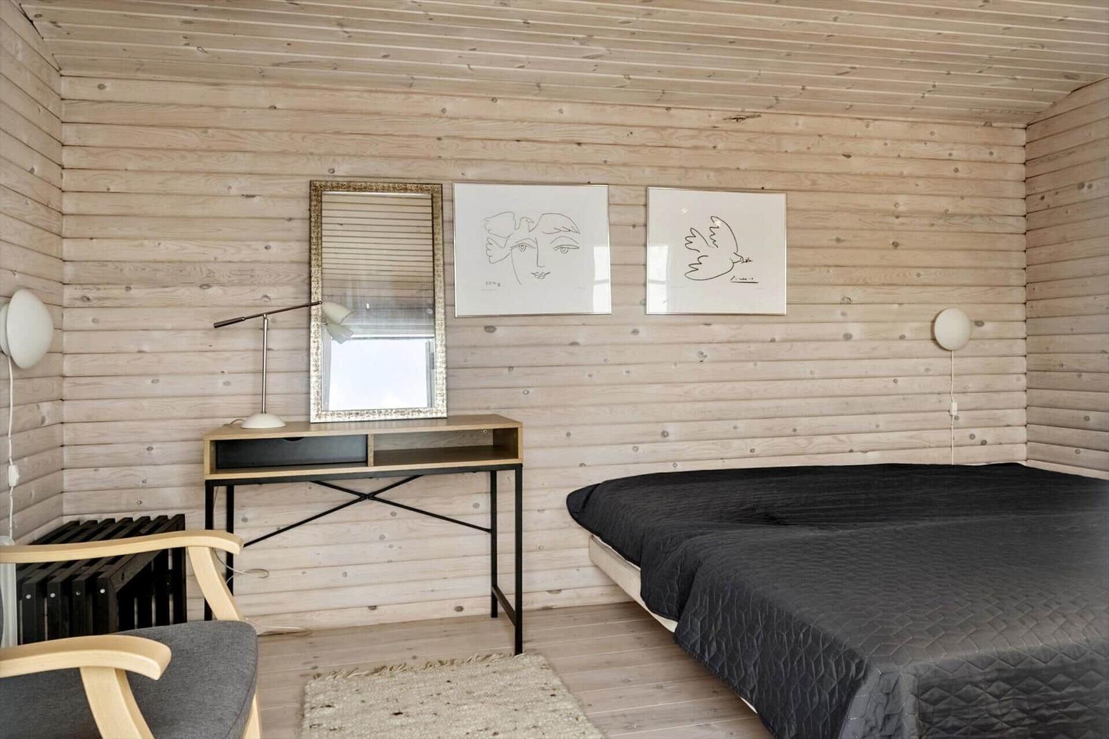 Schlafzimmer mit Holzwand, Bett, Schreibtisch und Spiegel.