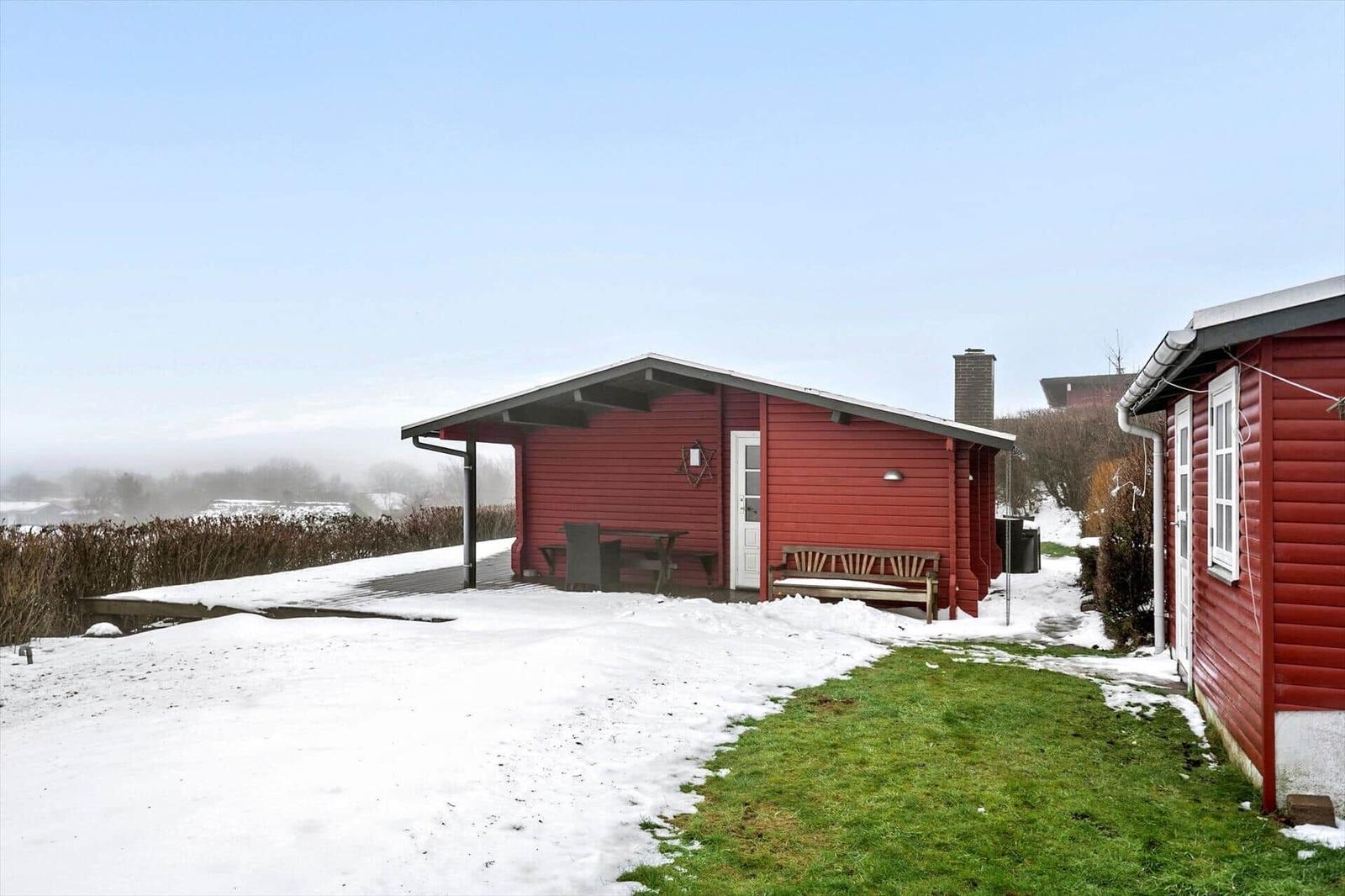Rotes Holzhaus mit Schneeflächen, Gartenbank und Tisch unter Dach.