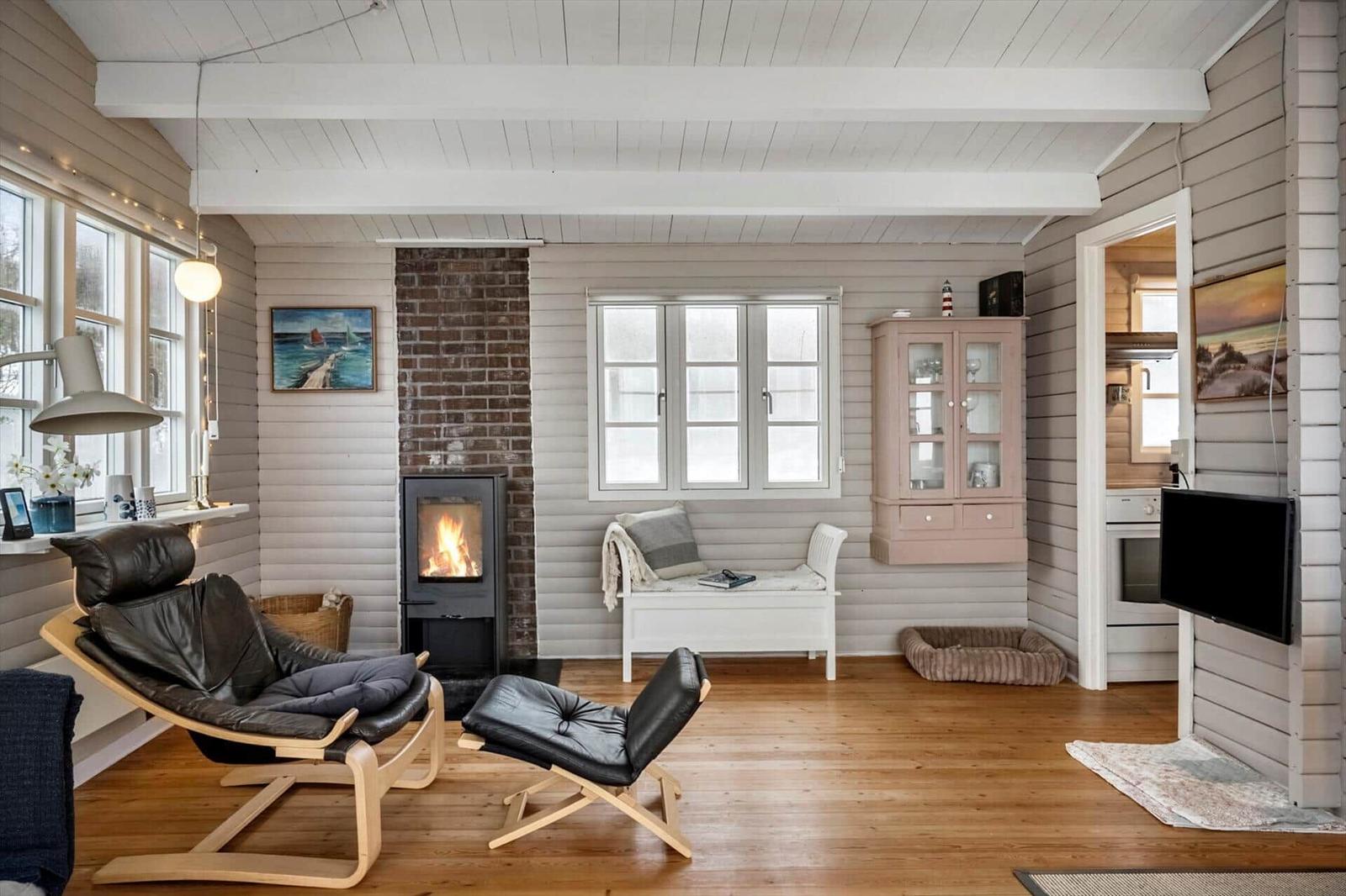 Wohnraum mit Kamin, Ledersessel und Fenstern. Küche und TV sichtbar.