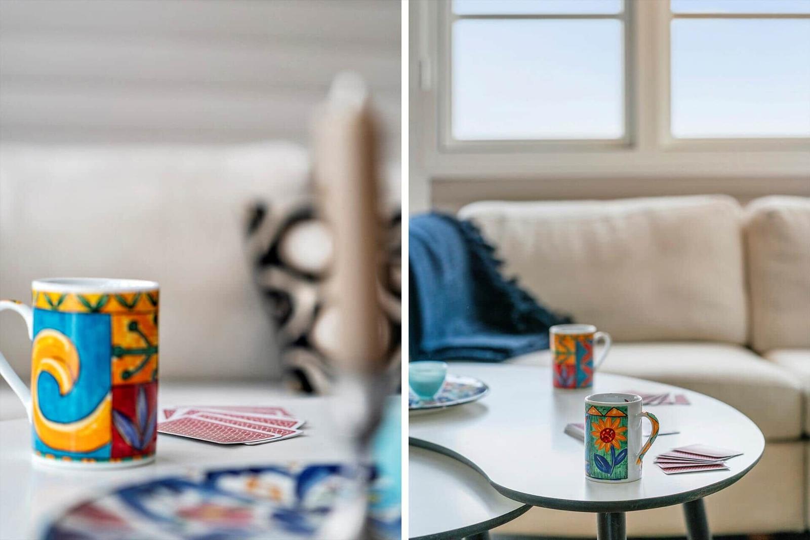 Tisch mit bunten Tassen und Karten vor einem Sofa mit blauem Decken.
